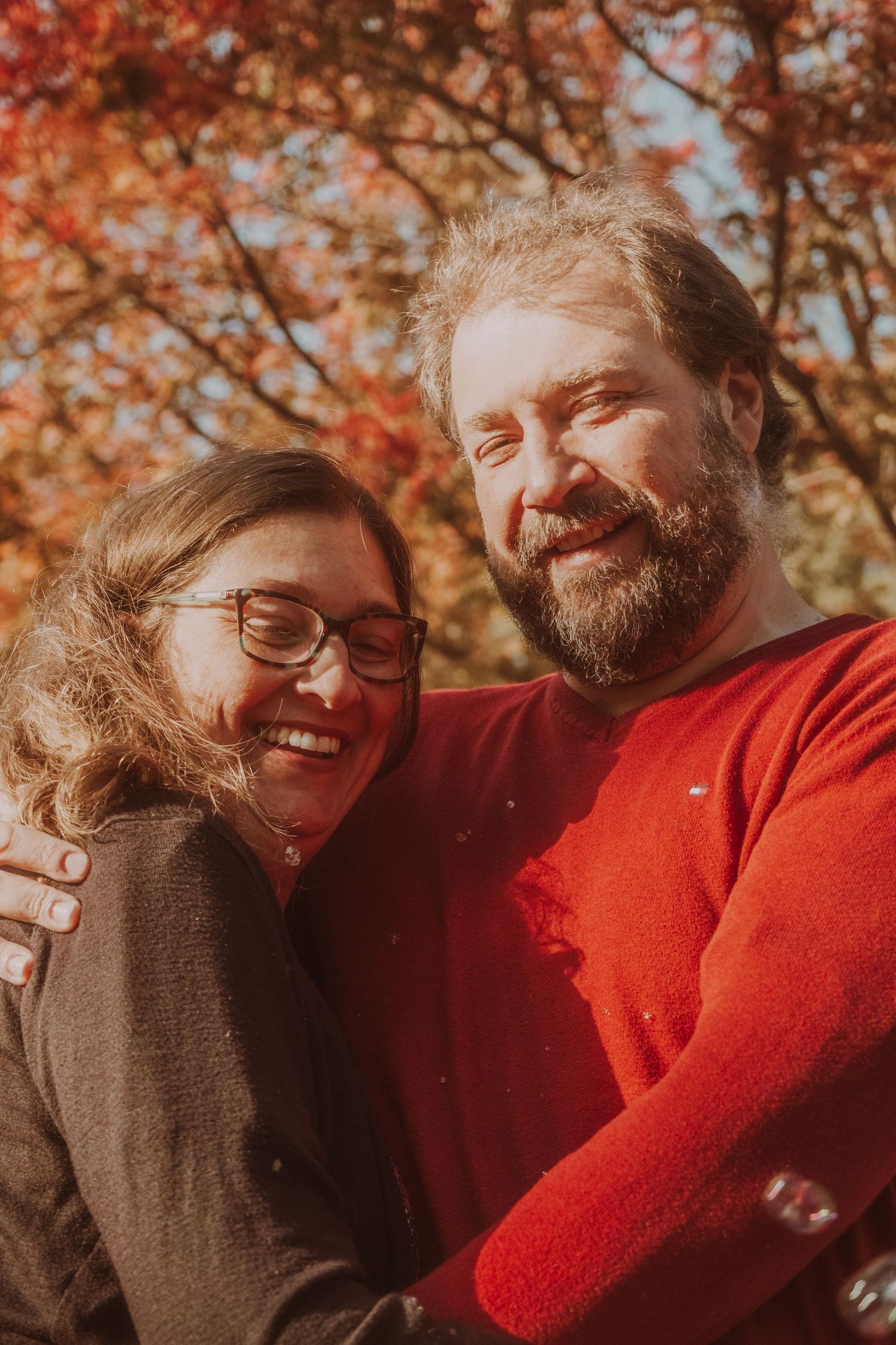 Couple sharing intimate moments against autumn foliage backdrop with warm lighting and red sweater.