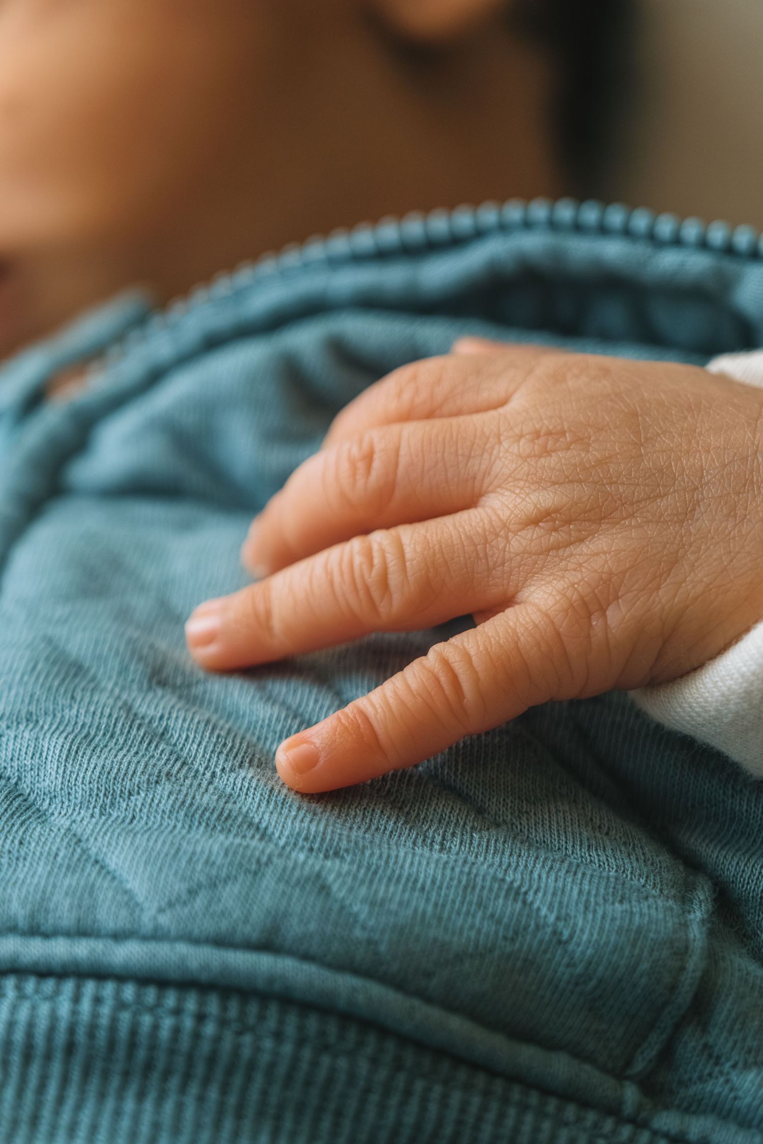 Adult hand gently resting on teal blue textured fabric in soft lighting.
