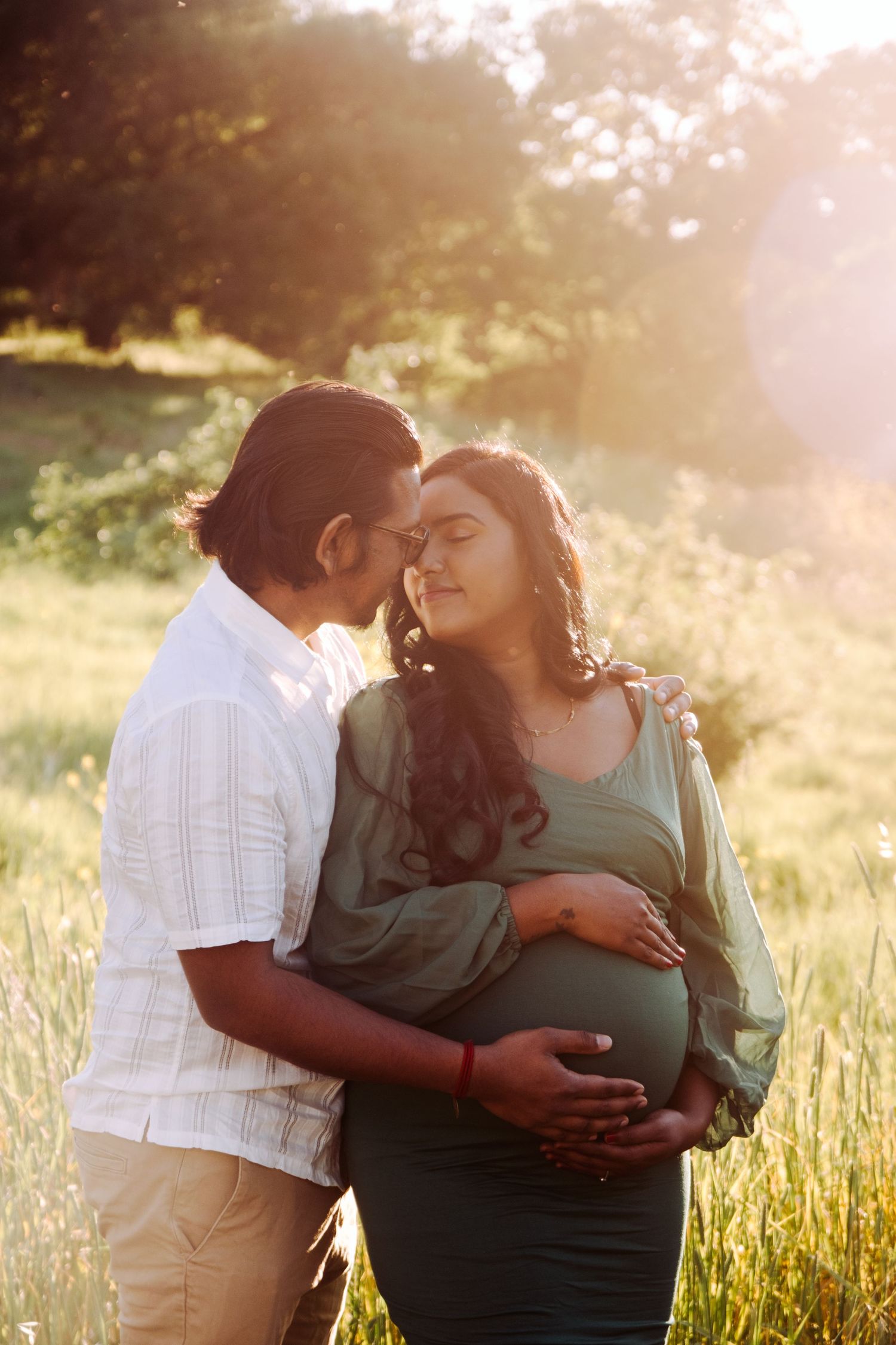 Couple sharing intimate moment in tall grass during golden hour.