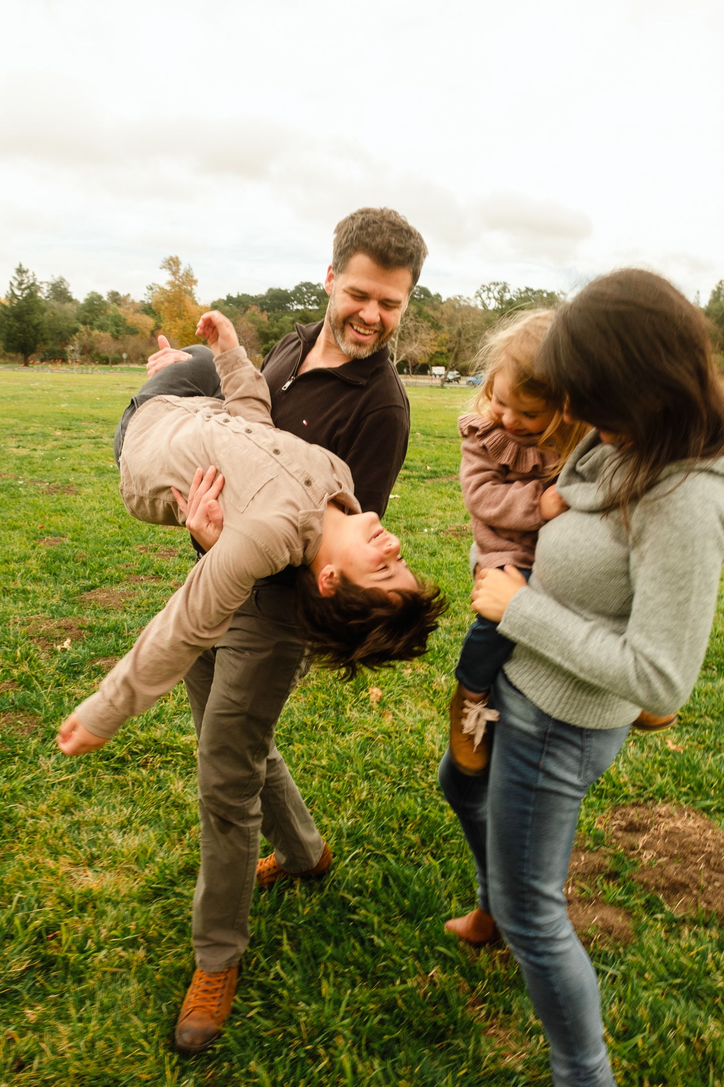 Couple performing dramatic dip dance move in green meadow on cloudy day.