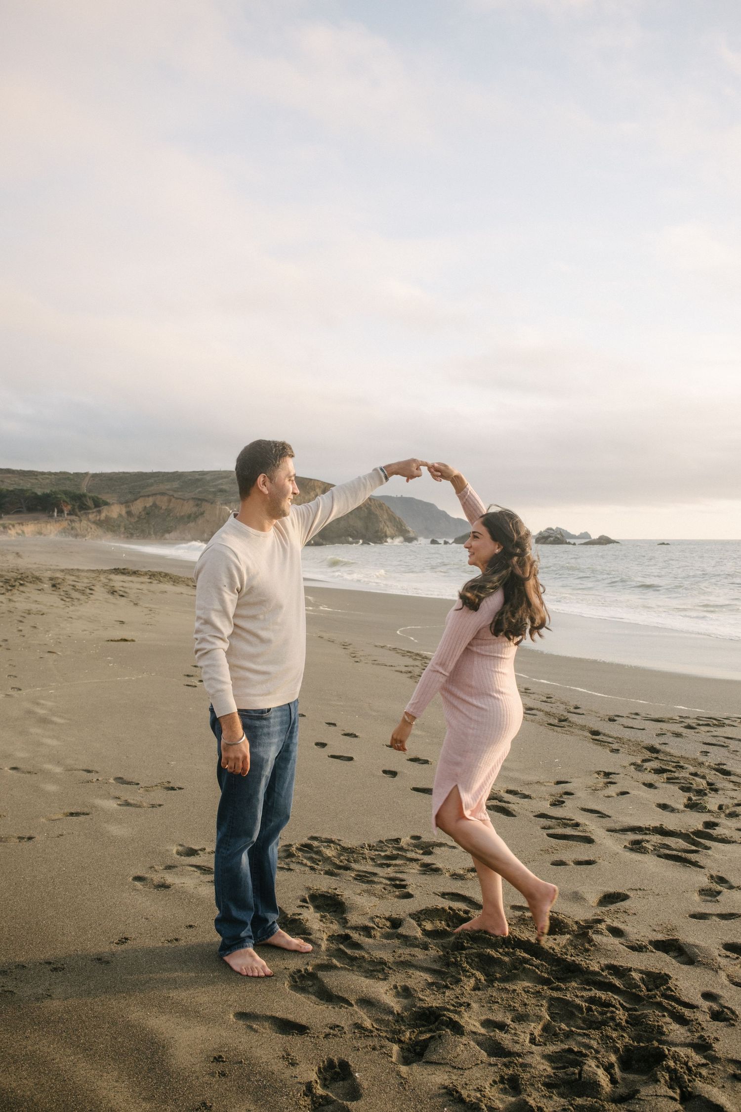 Playful couple interacting on a rocky beach during golden hour with coastal cliffs in view.