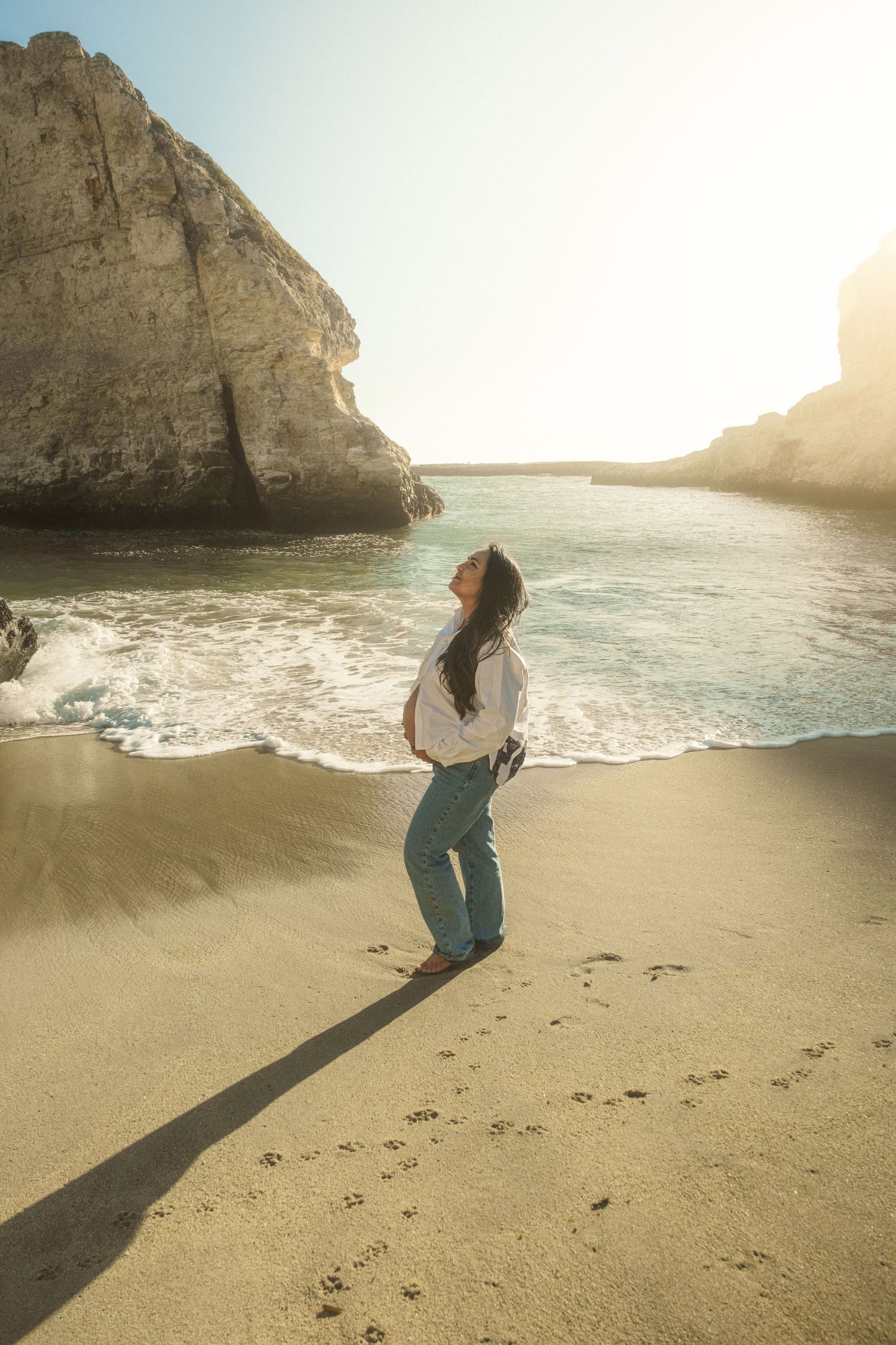 Person walking along a scenic beach at sunset with dramatic coastal cliffs and ocean waves.