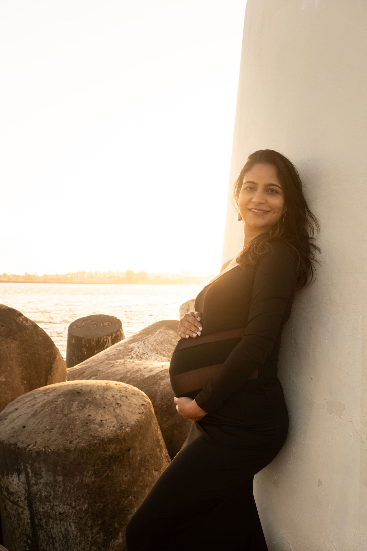 Maternity portrait session against white wall with sunset glow.