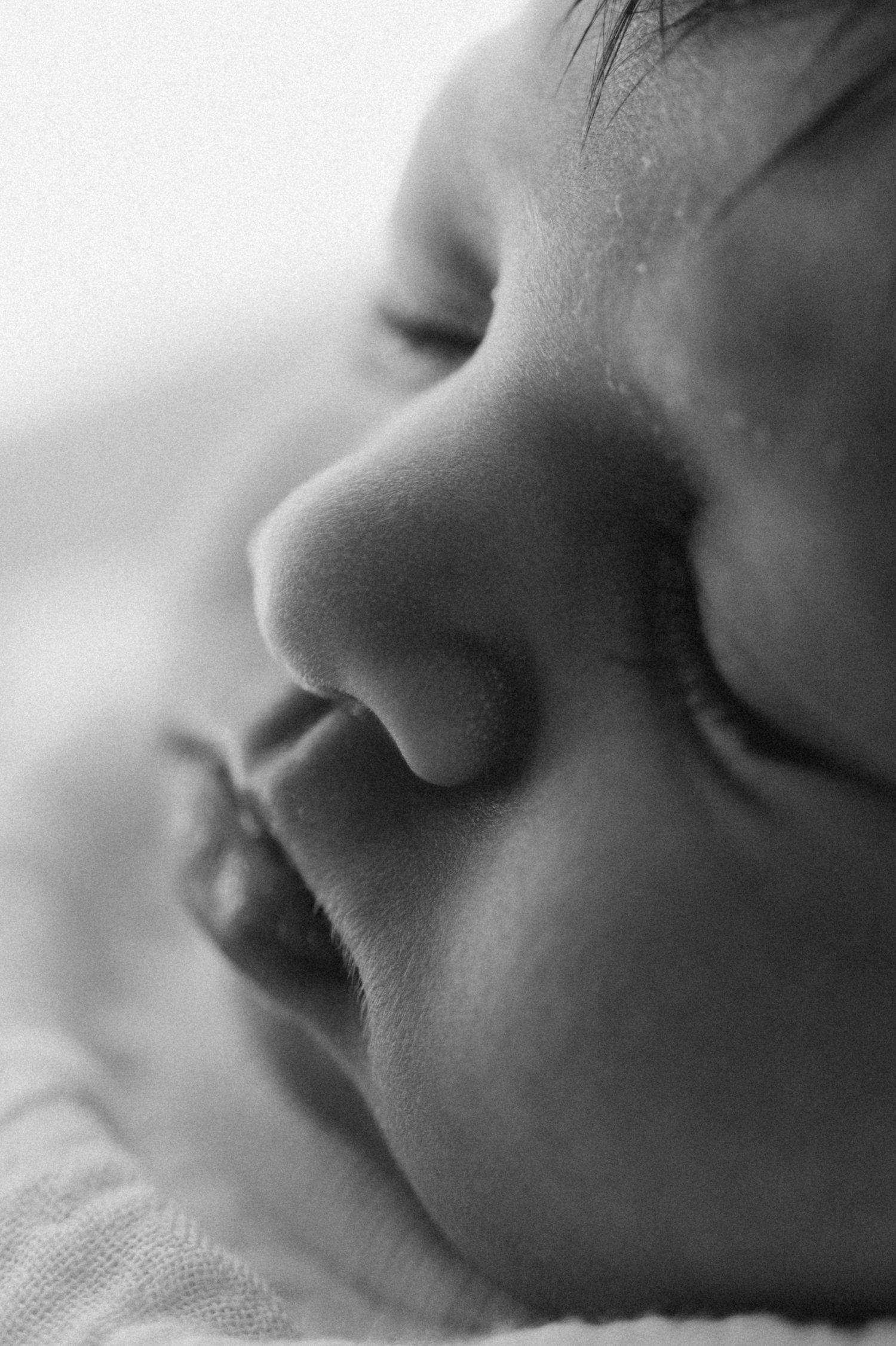 Close-up black and white photo of a sleeping newborn baby's face, capturing delicate features in soft focus.