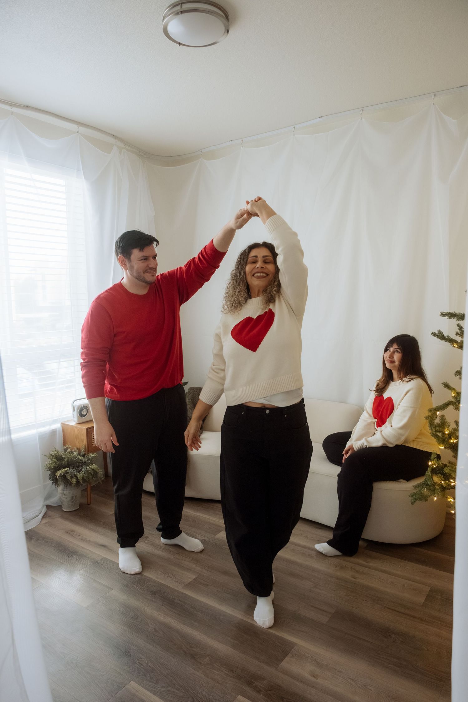 Playful dance poses in coordinated red and white outfits by decorated Christmas tree.