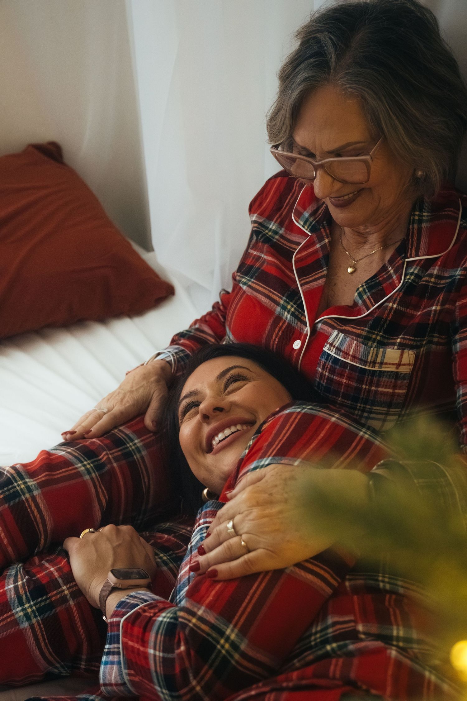 Two people in matching plaid pajamas share joyful moment by Christmas tree lights.