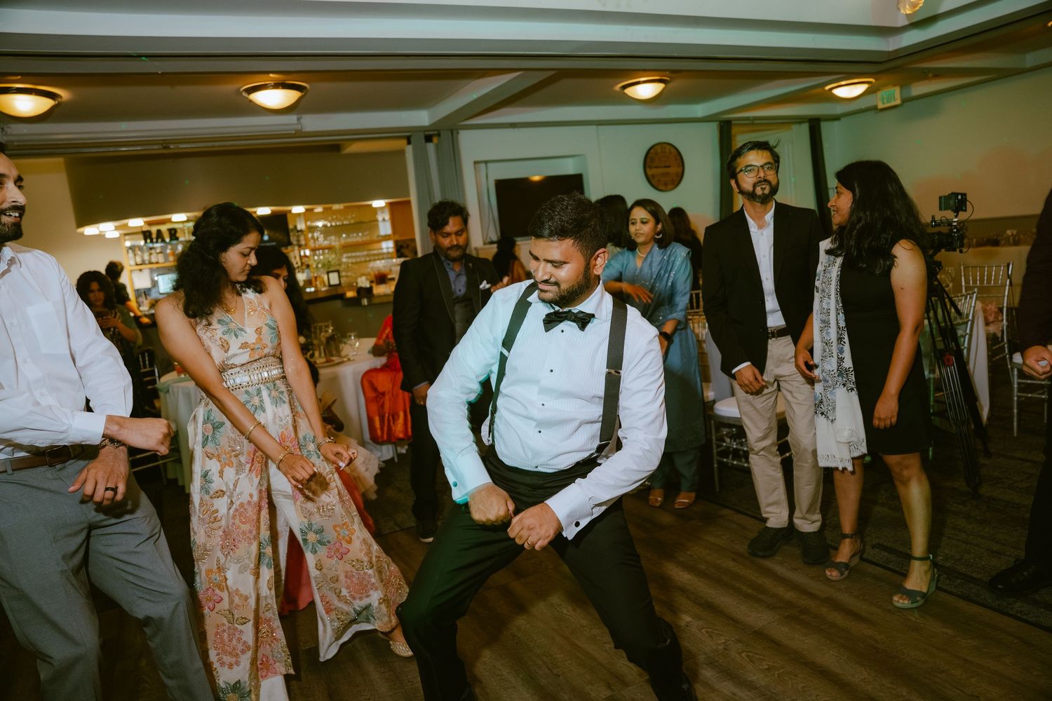 Guests dancing energetically at a wedding reception on a wooden dance floor in a decorated venue.
