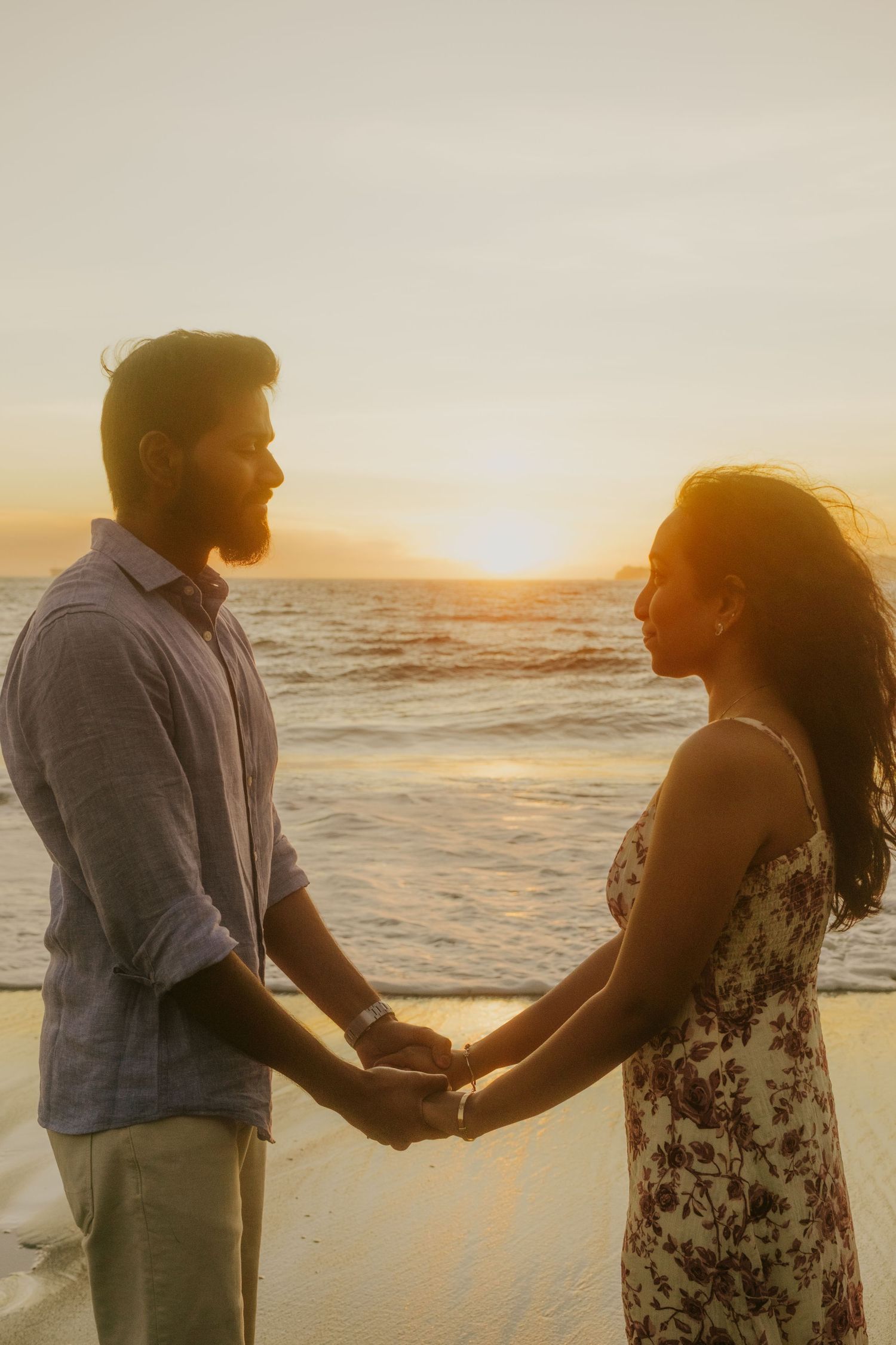 Two people holding hands on the beach at sunset with waves crashing behind them.