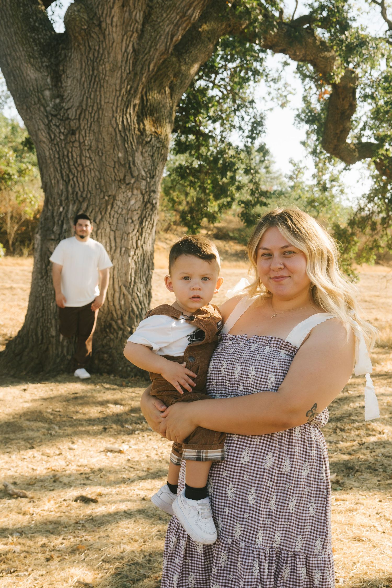 A family portrait session under large oak trees during golden hour.