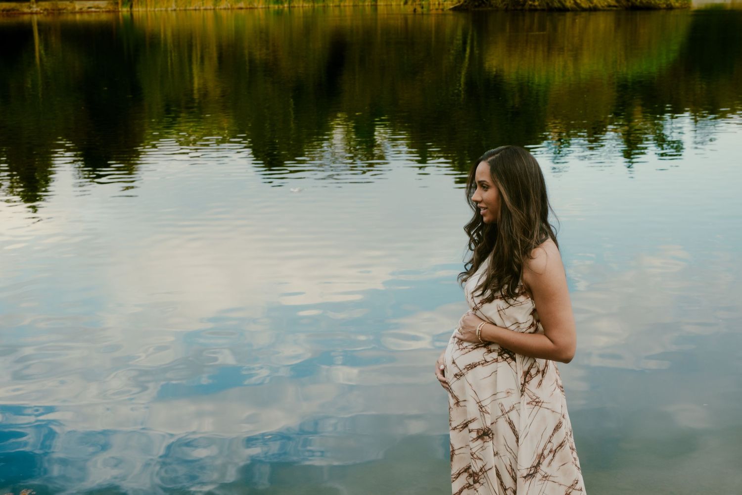 Person in patterned dress poses gracefully by a lake with golden reflections.