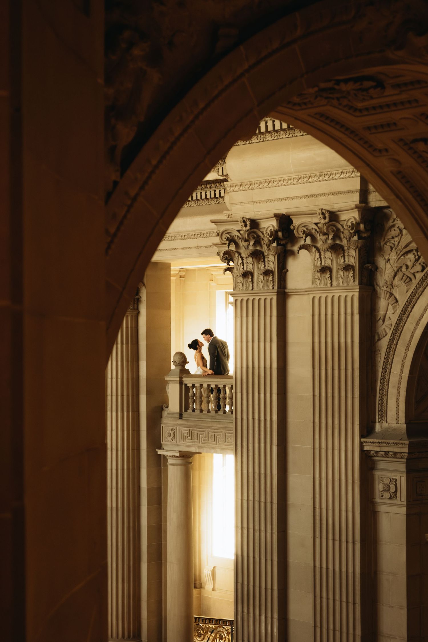 Ornate classical columns and arches line a grand hallway with dramatic lighting in an elegant architectural interior.