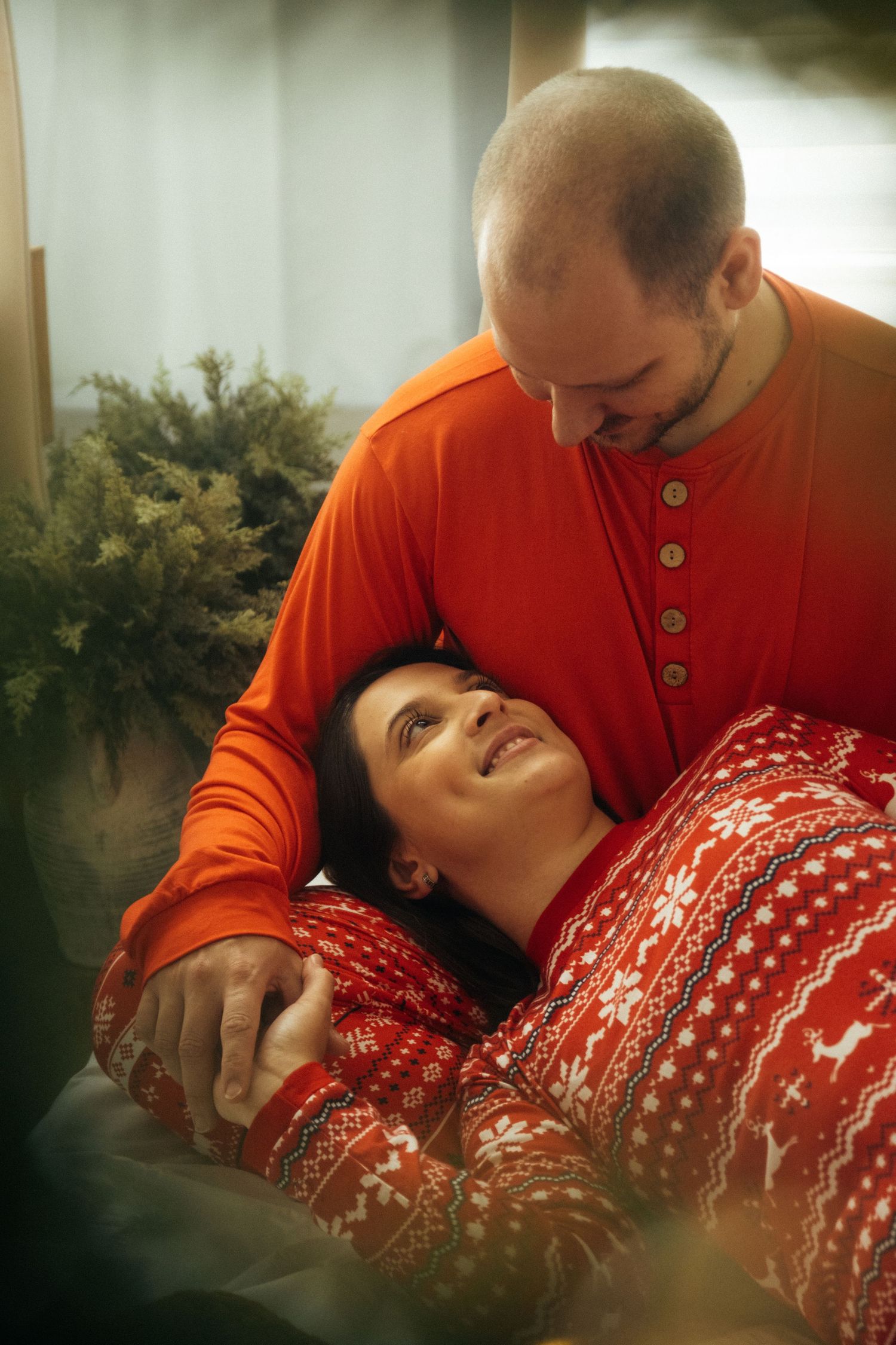 Intimate holiday moment captured with matching festive sweaters beside a decorated Christmas tree.