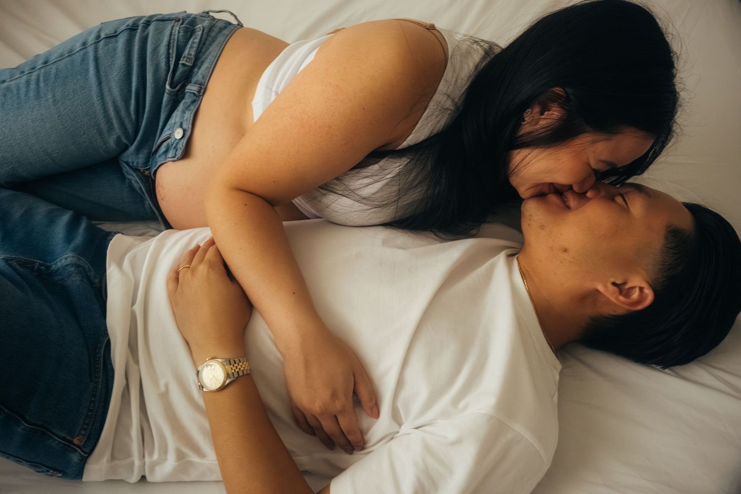 Intimate couple's portrait on white bedding during pregnancy photoshoot.