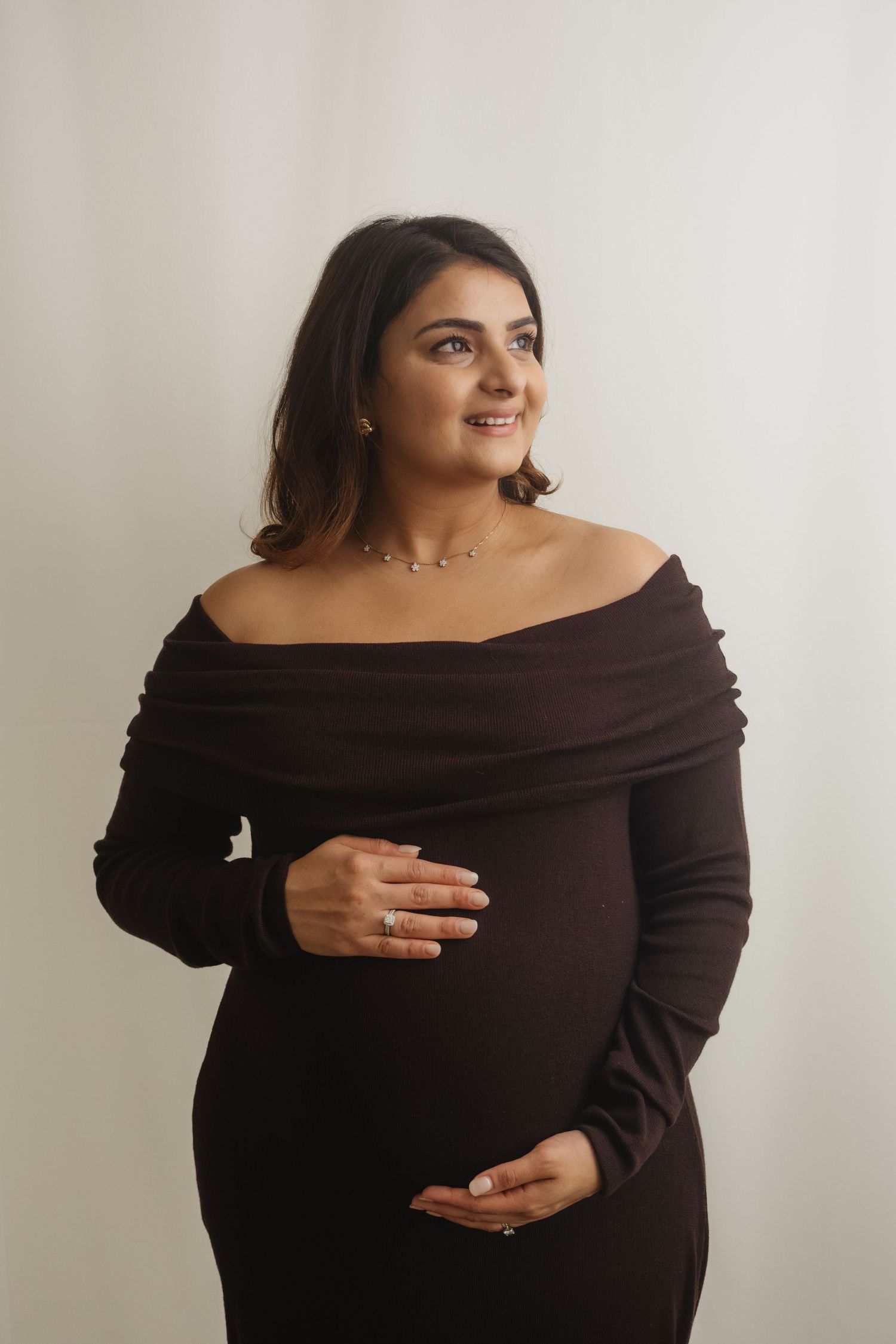 A woman in a brown off-shoulder dress poses for maternity photos.