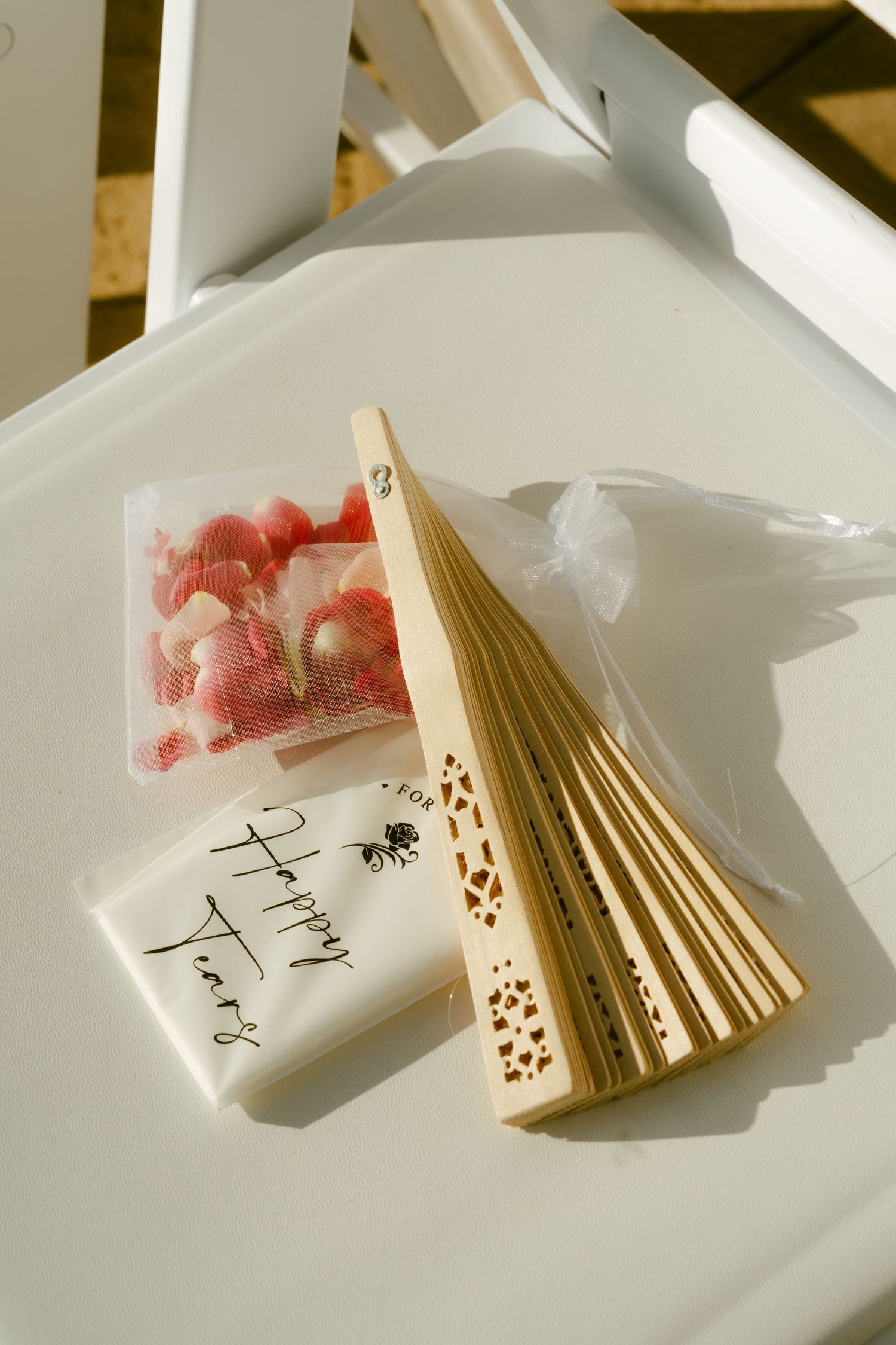 Wedding favor items including a decorative fan, candy, and Happy Years soap on a white chair.