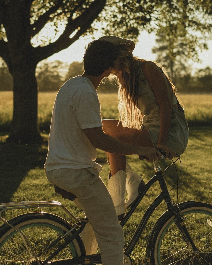 Couple sharing tender moments while riding bicycles at sunset in a tree-lined park.