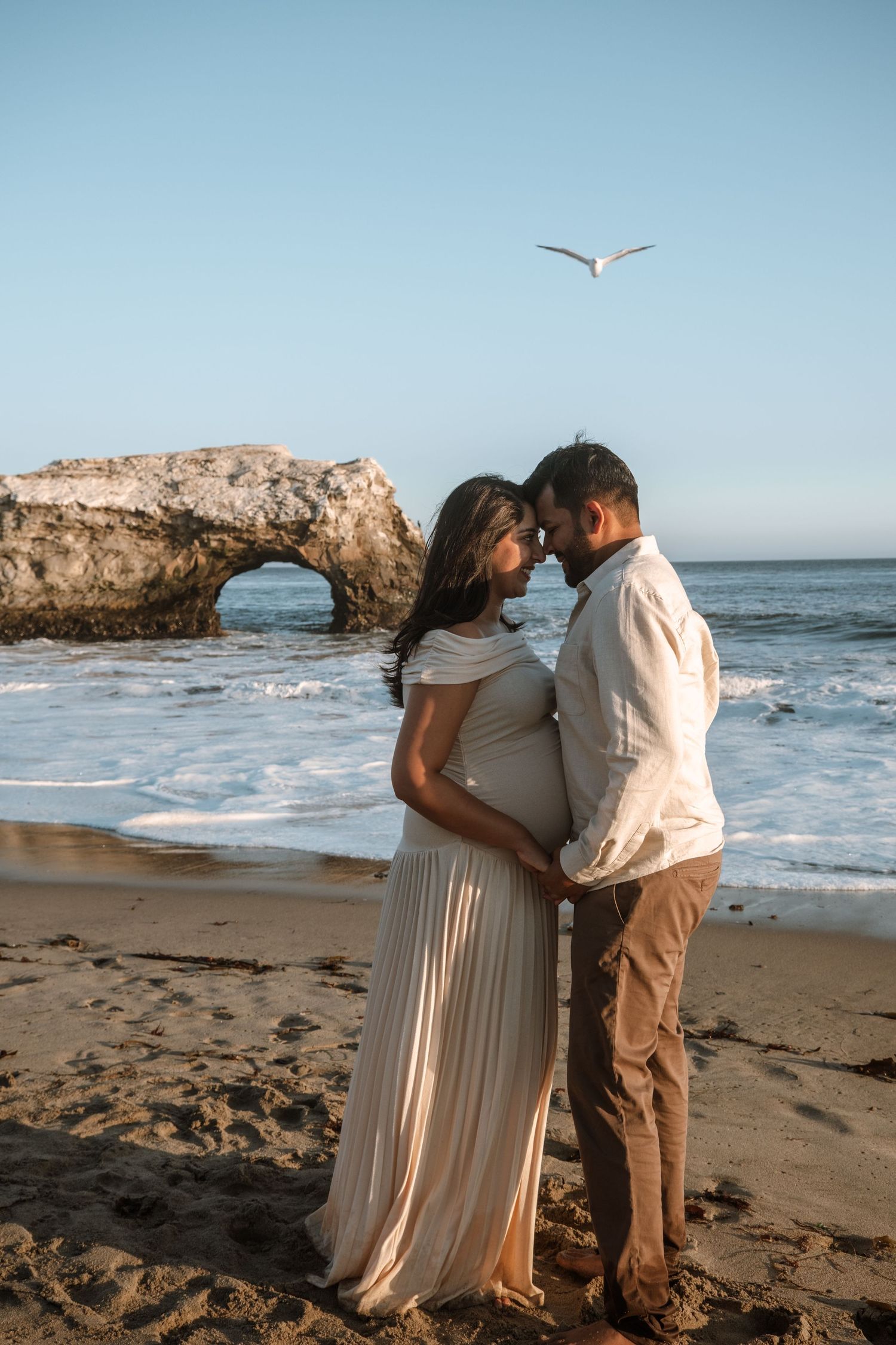Romantic beach photoshoot with seagulls flying overhead near rocky coastal formations.