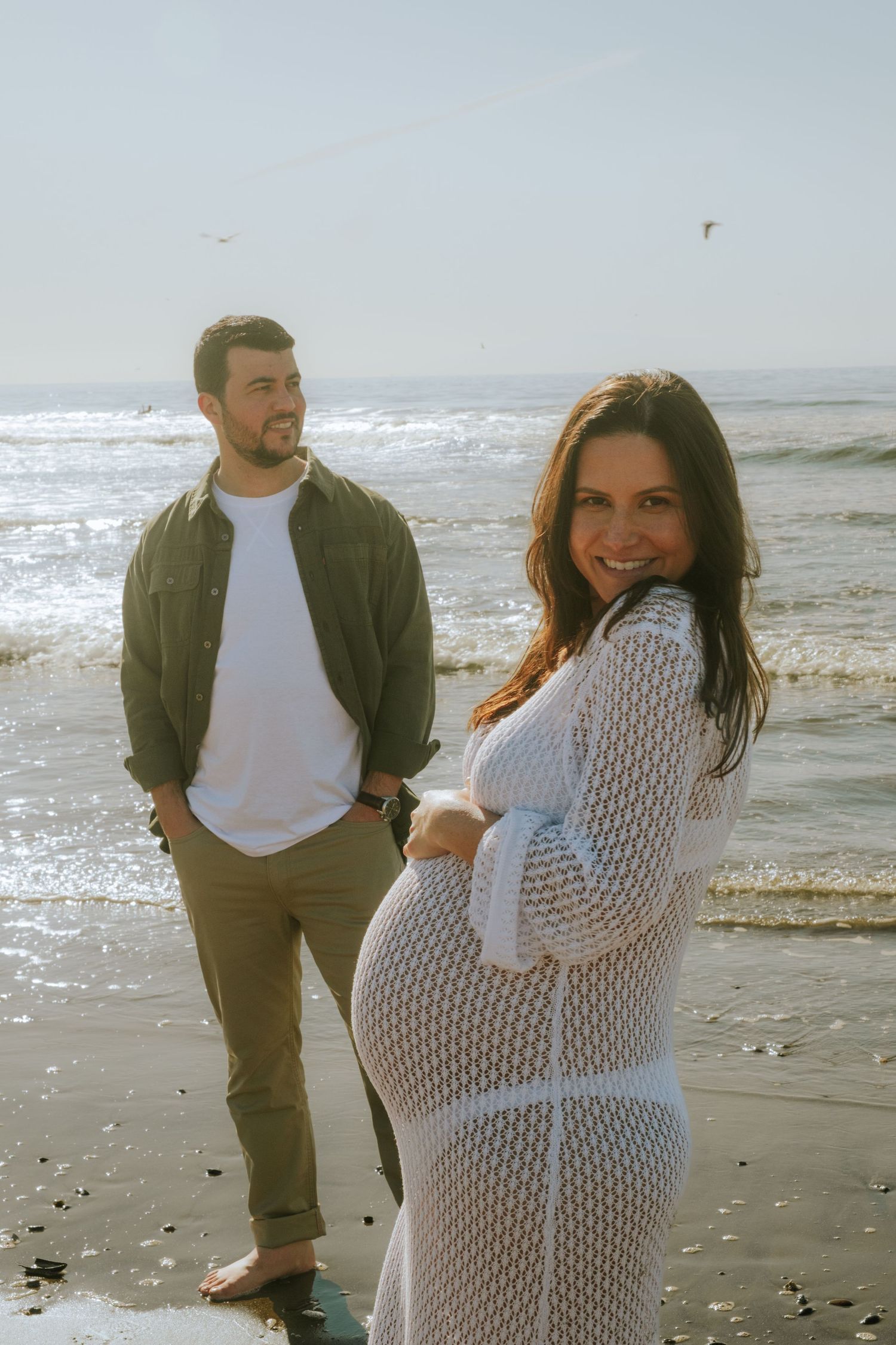 A couple in casual attire enjoys a playful moment together on the beach.