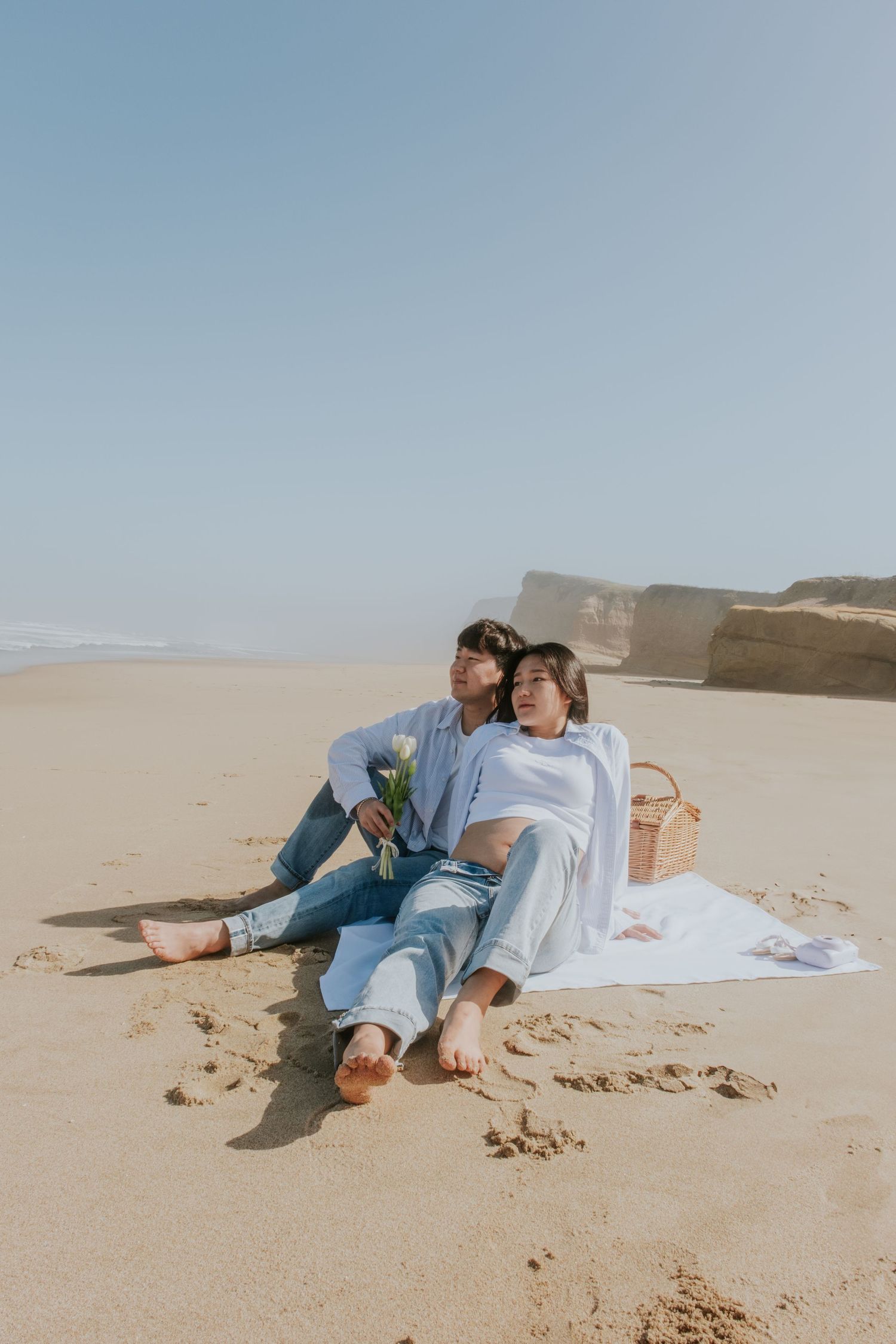 A couple lounges on a blanket during a romantic beach photoshoot.