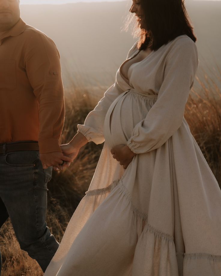 Maternity photo showing silhouette of couple in white dress against sunset backdrop.