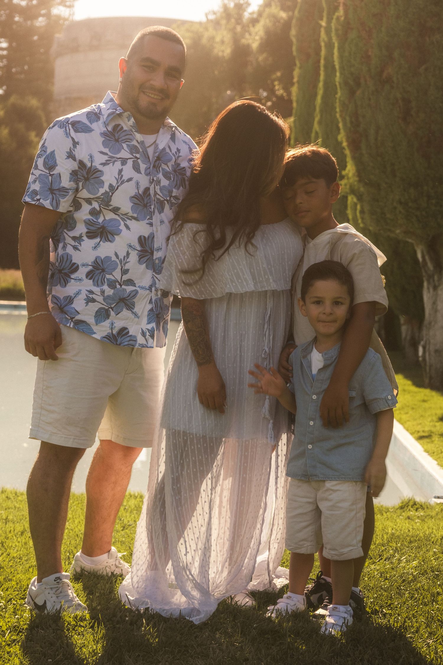 A family group poses together on grass during golden hour wearing coordinated blue and white outfits.