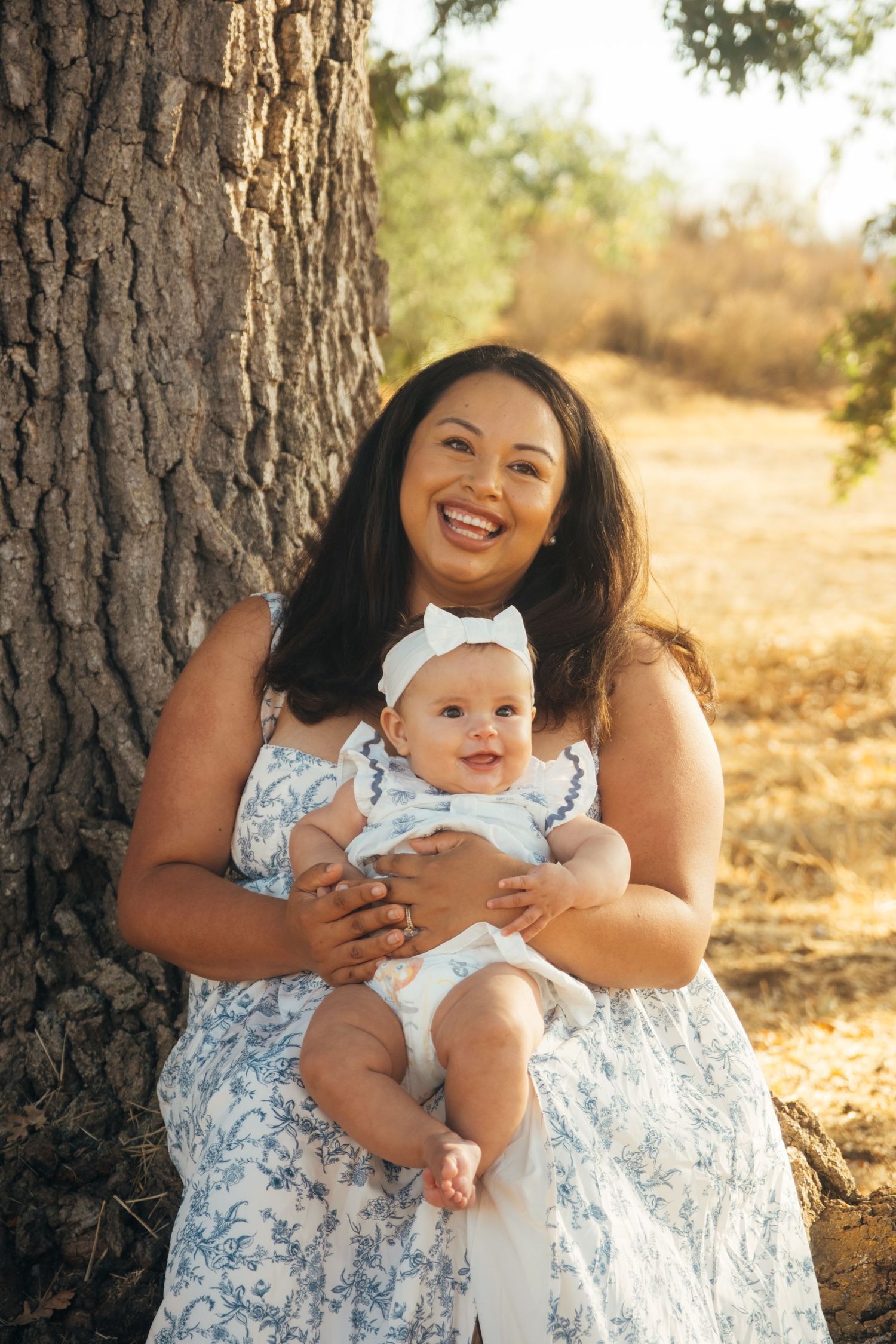 Mother and baby in floral dress share happy moment during outdoor photoshoot.