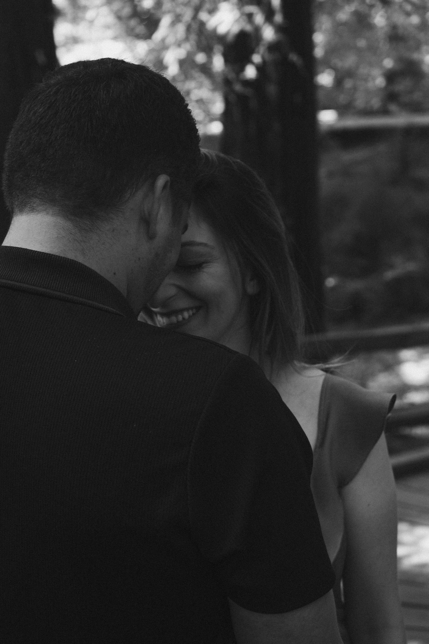 A romantic couple shares an intimate moment in black and white on a wooded path.