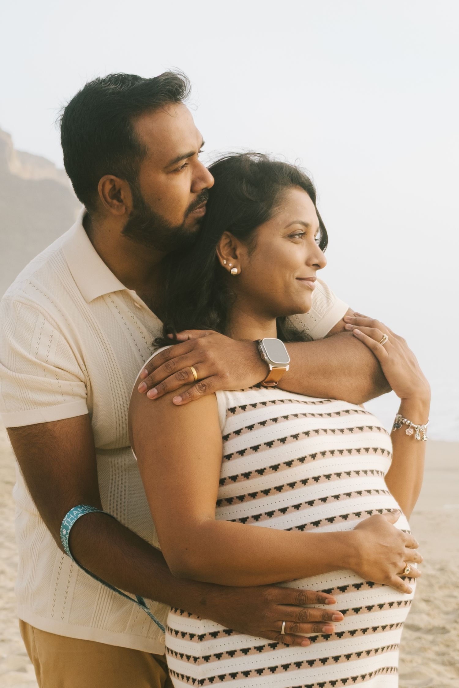 A couple shares an intimate embrace during a beach maternity photoshoot.
