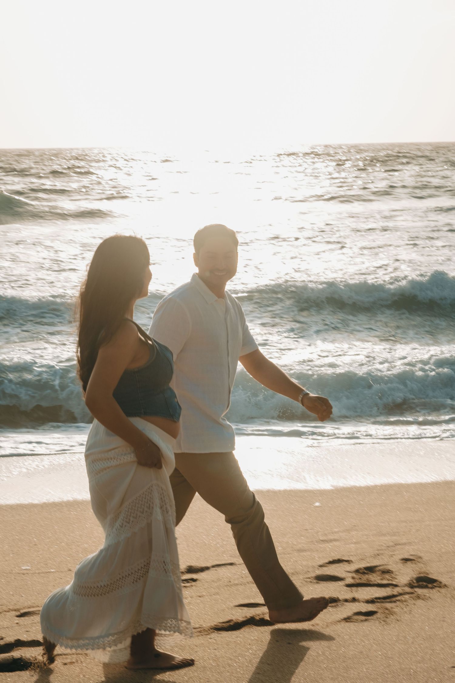 A couple walks along the shoreline during golden hour at the beach.