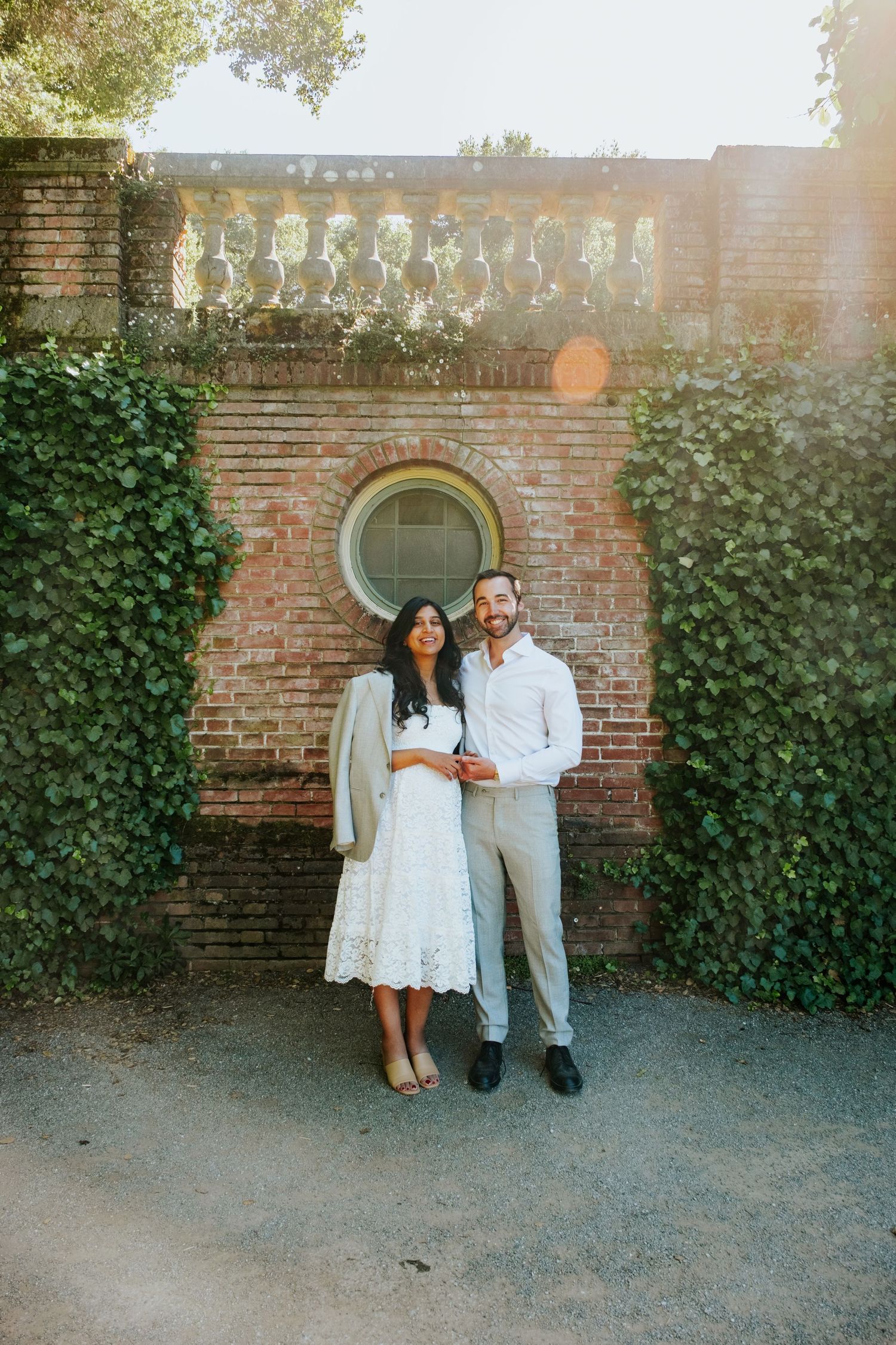 Couple standing against ivy-covered brick wall in garden setting.