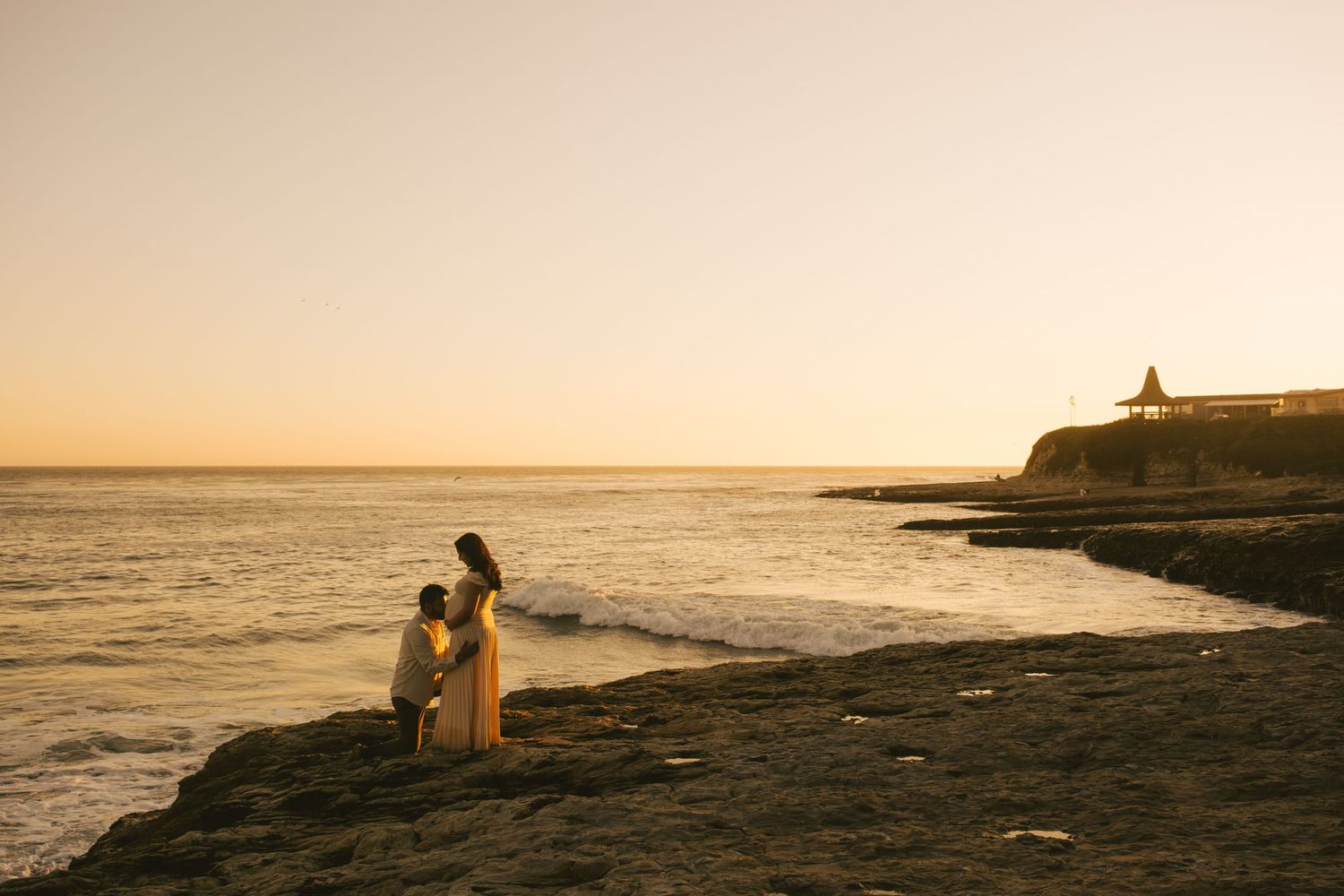 Scenic sunset beach landscape with warm golden light and distant lighthouse.