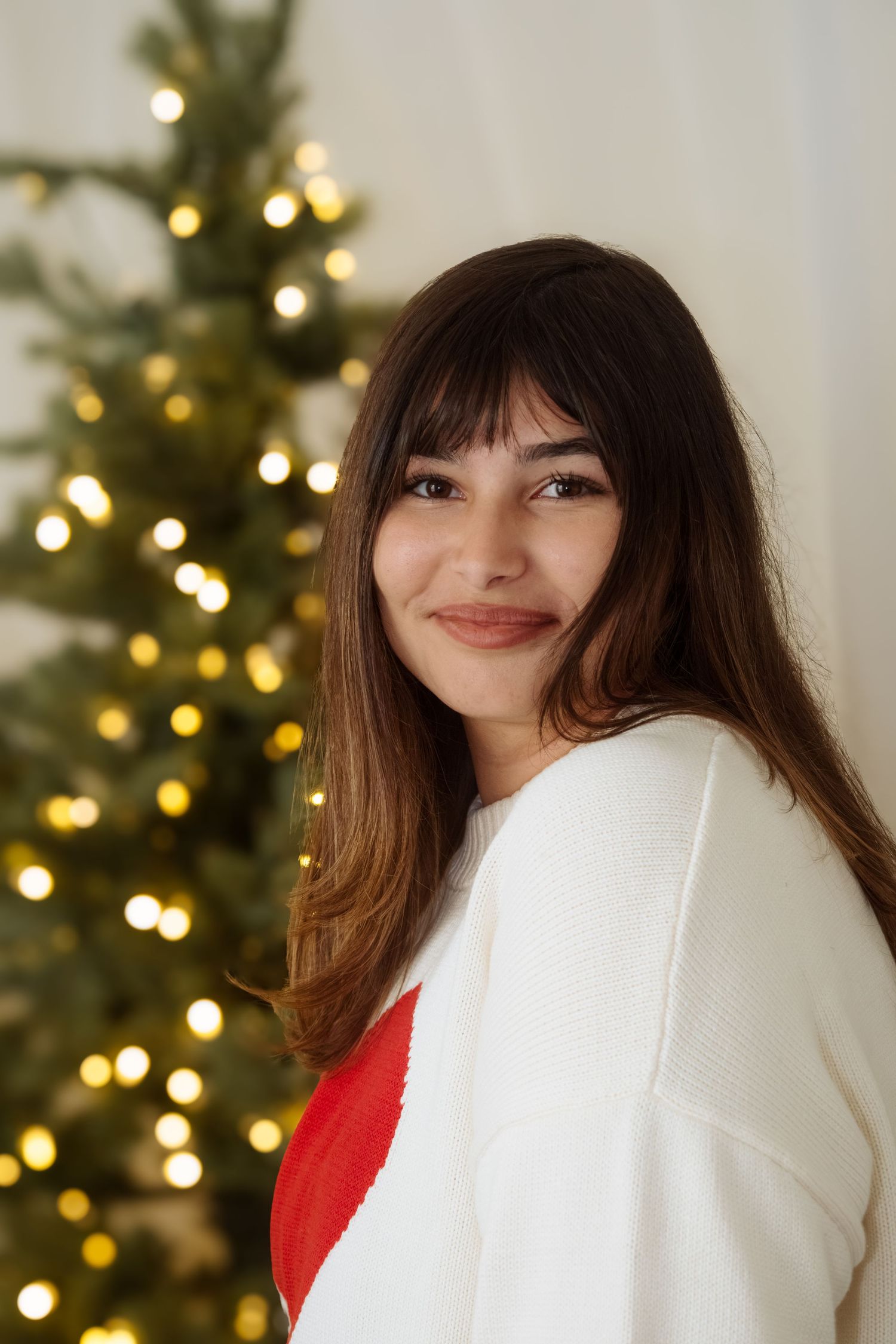 Cozy winter portraits with white sweater and Christmas tree backdrop.