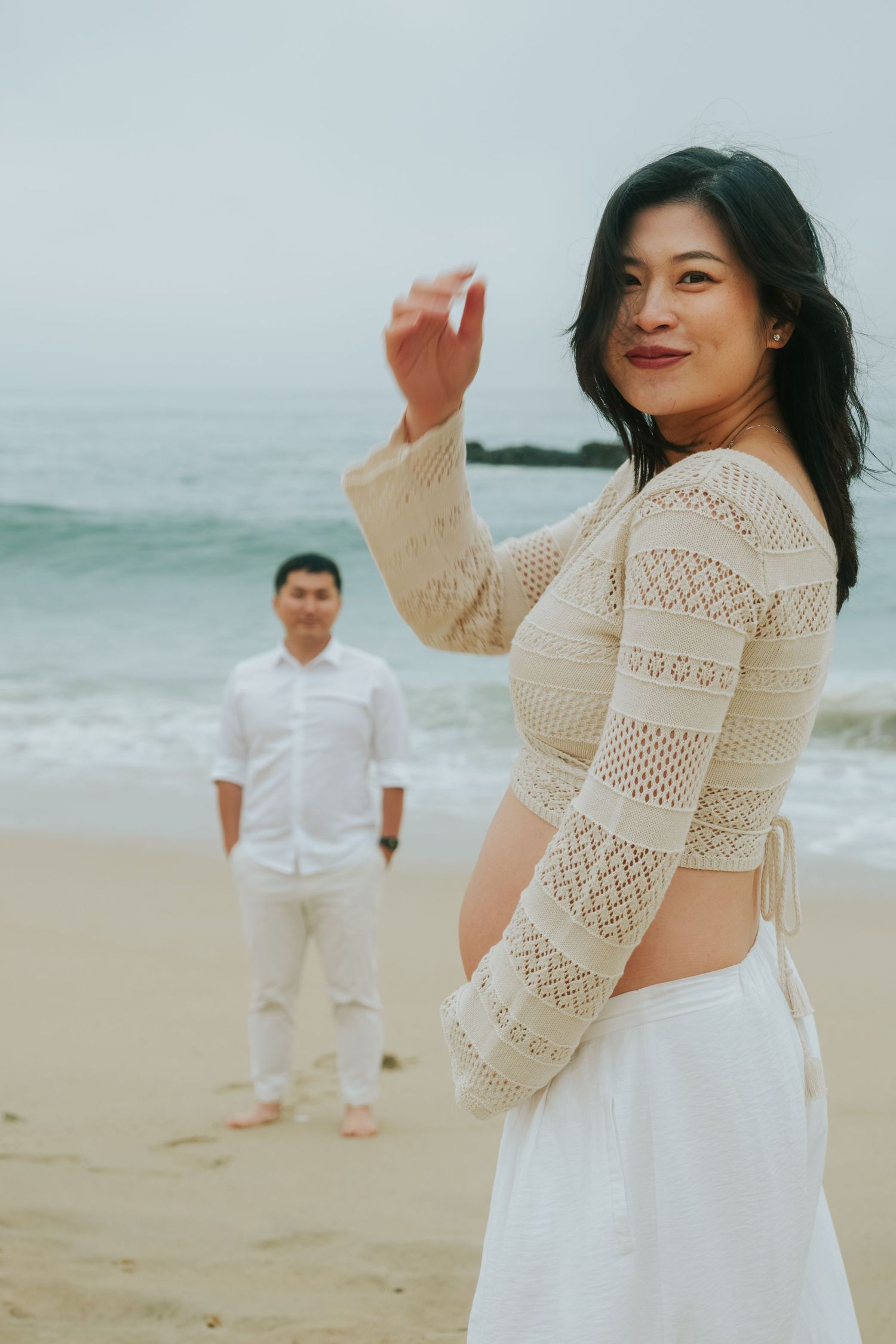 Playful beach photoshoot featuring a couple in white outfits dancing and laughing on the sand.