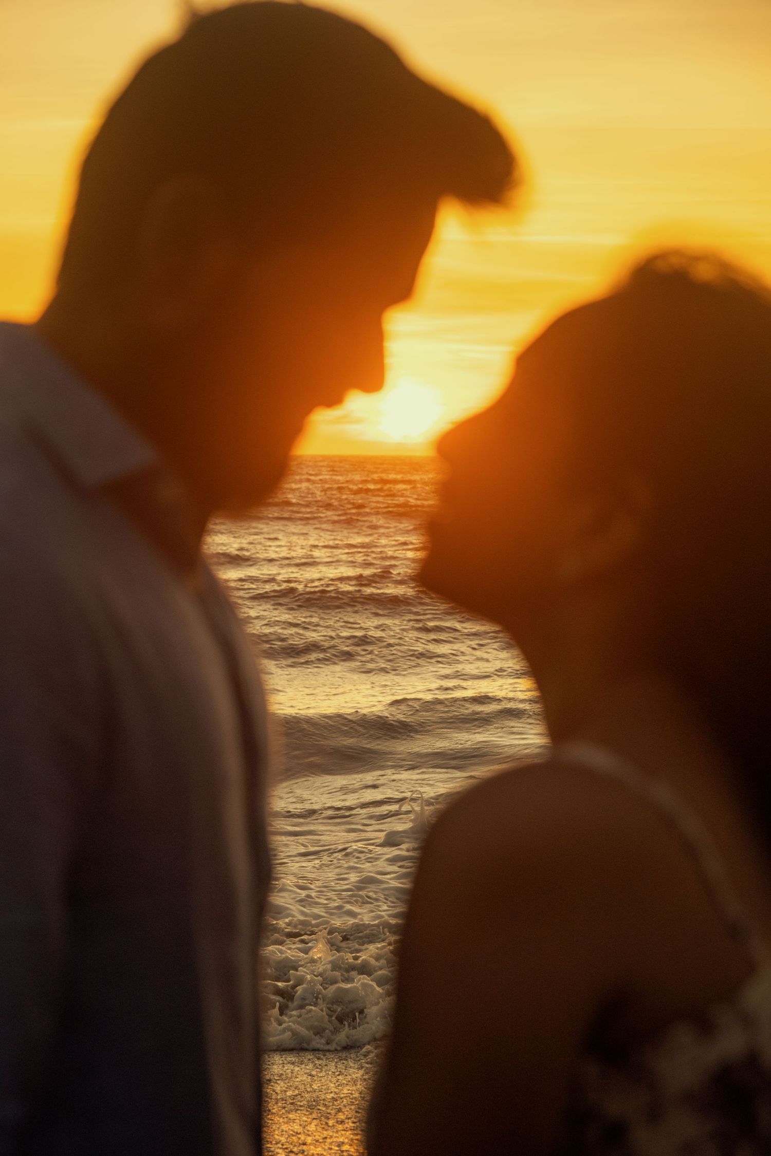 Silhouettes of a couple against a dramatic orange sunset at the beach.