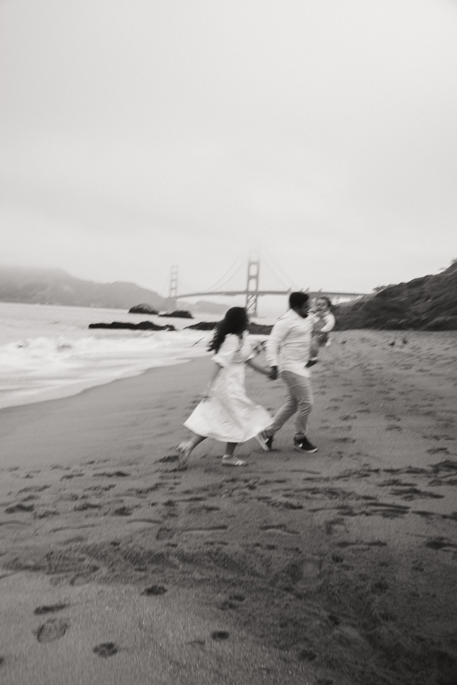 A family runs and plays on a beach with the Golden Gate Bridge visible in the distance.