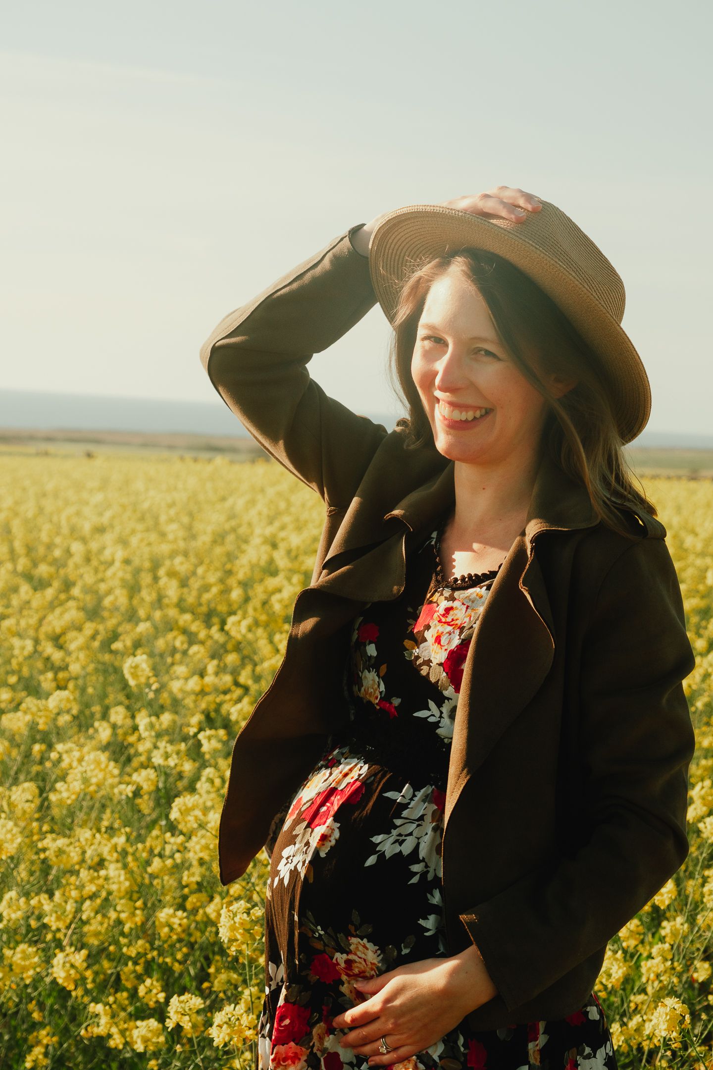 A joyful woman in a sunhat laughs while standing in a bright yellow canola flower field.