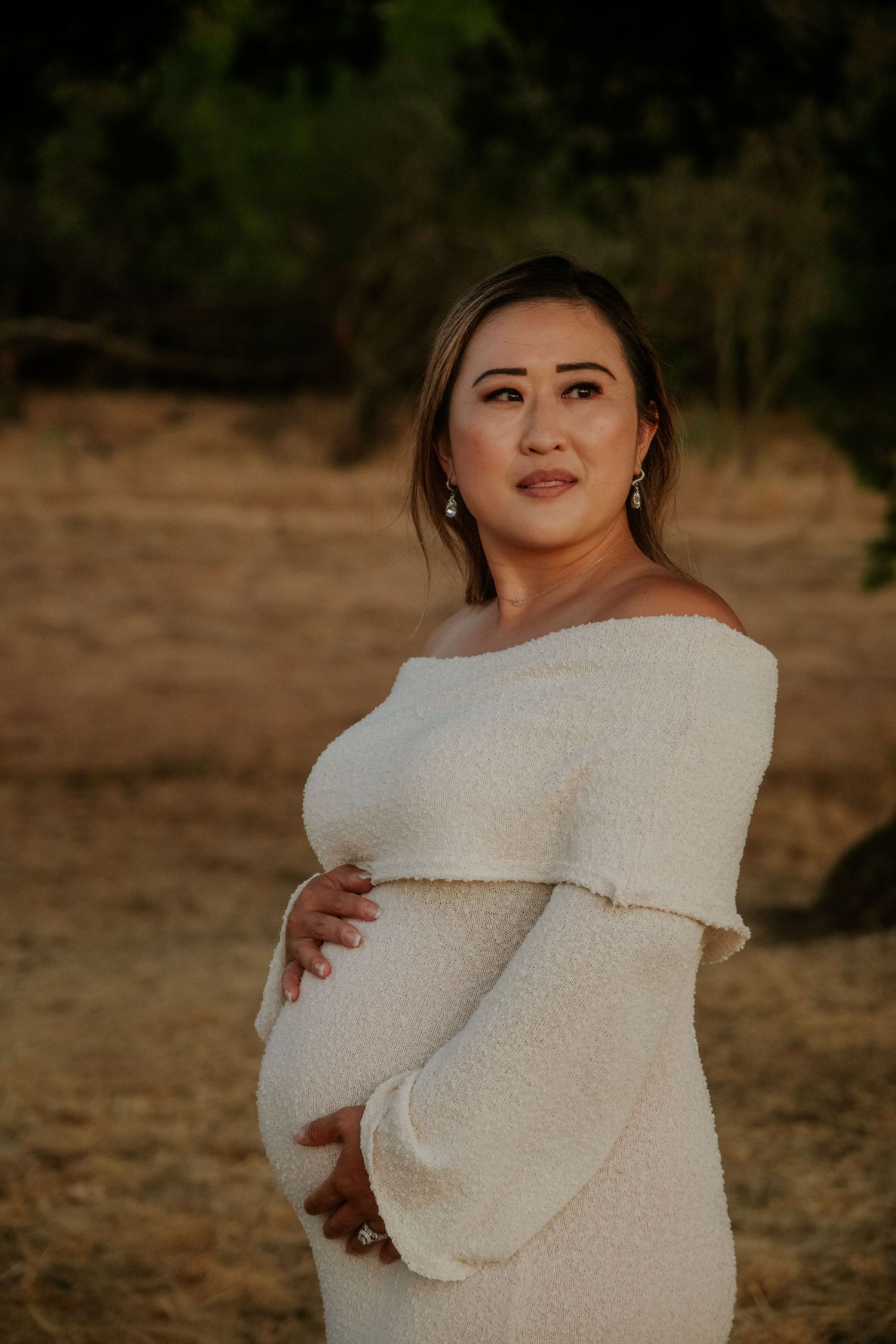 A person wearing a white sweater poses outdoors during golden hour.