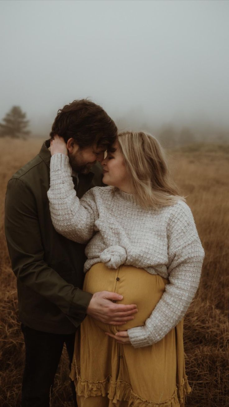A couple embraces in a misty field with golden grass and moody atmosphere.