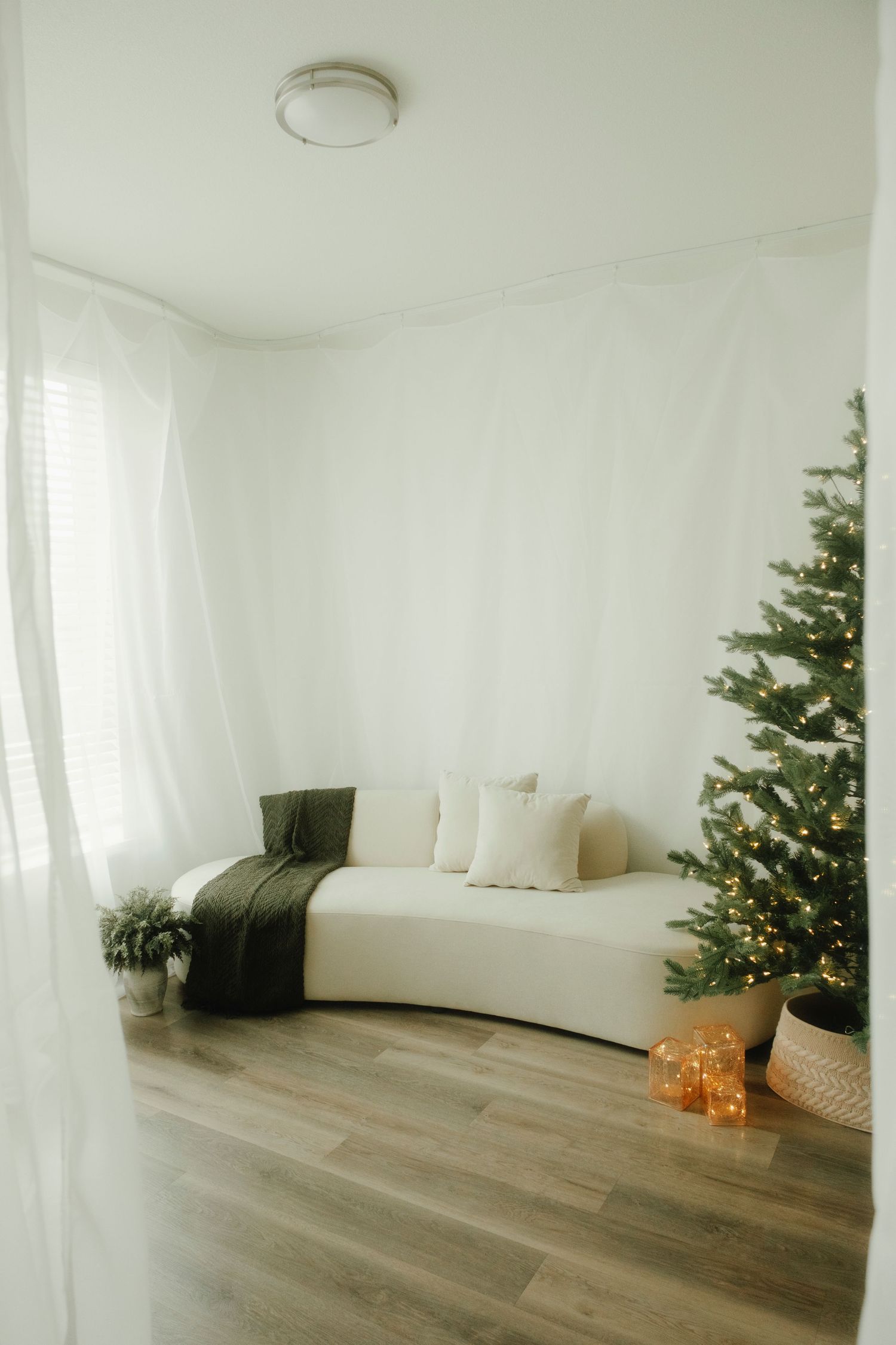 Modern white interior with Christmas tree, white sofa, and hardwood flooring.