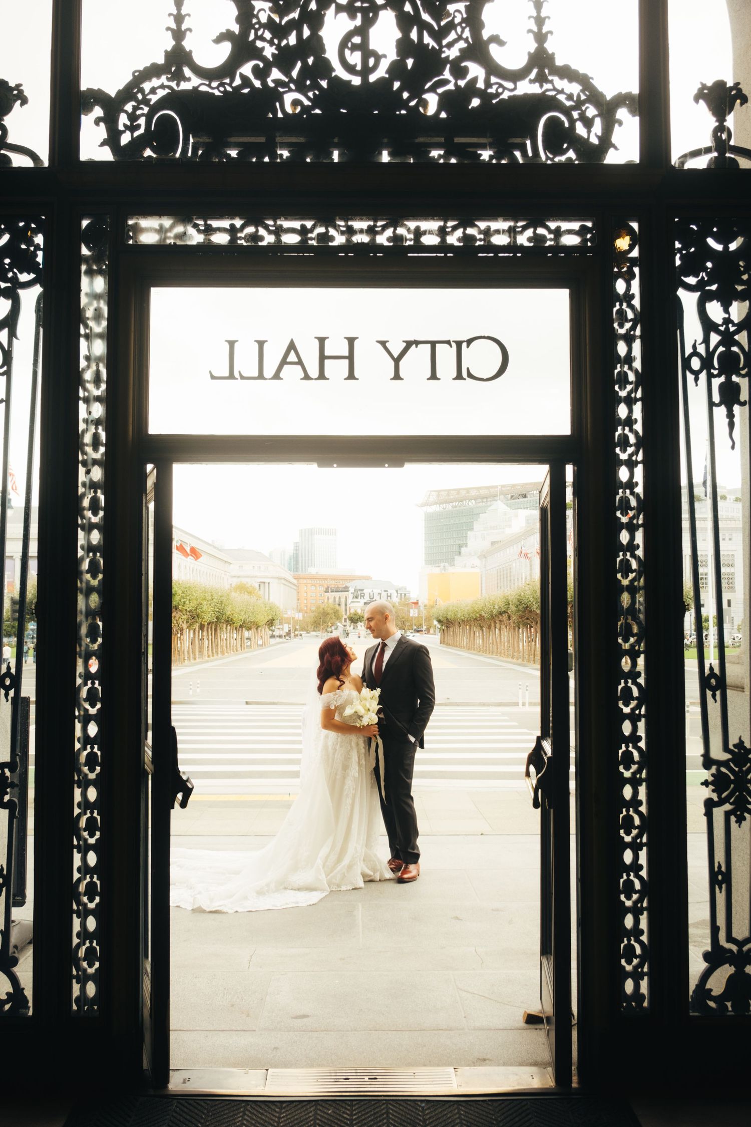 Newlyweds pose in ornate doorframe of City Hall with decorative ironwork details.