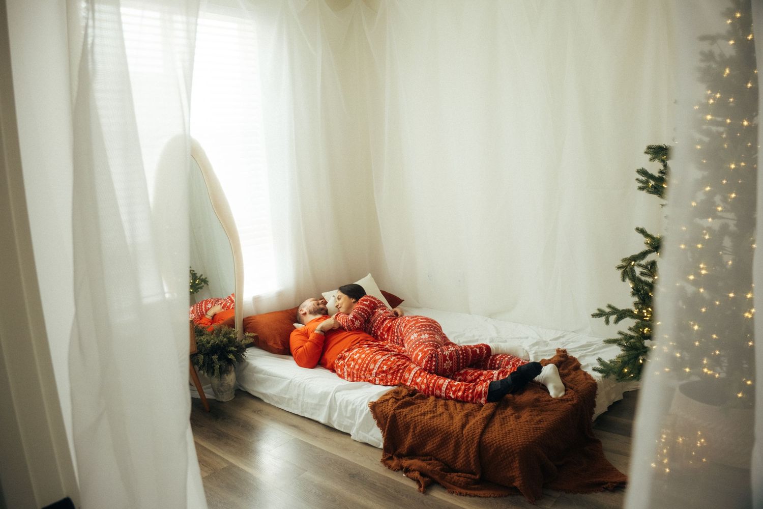 A festive bedroom setting with Christmas tree lights and cozy red holiday bedding.