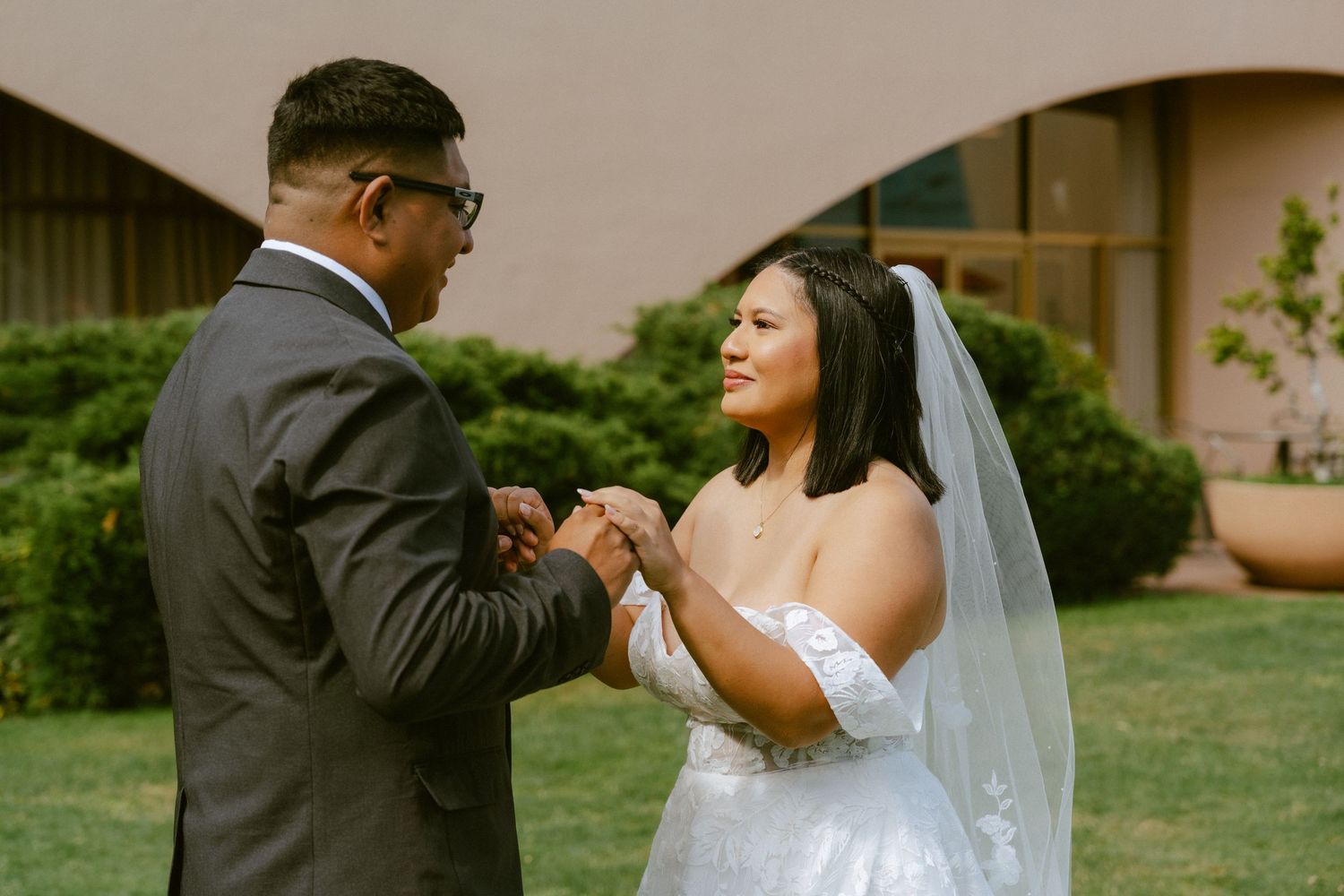 Bride and groom exchange rings outdoors during wedding ceremony, bride wearing white gown and veil.