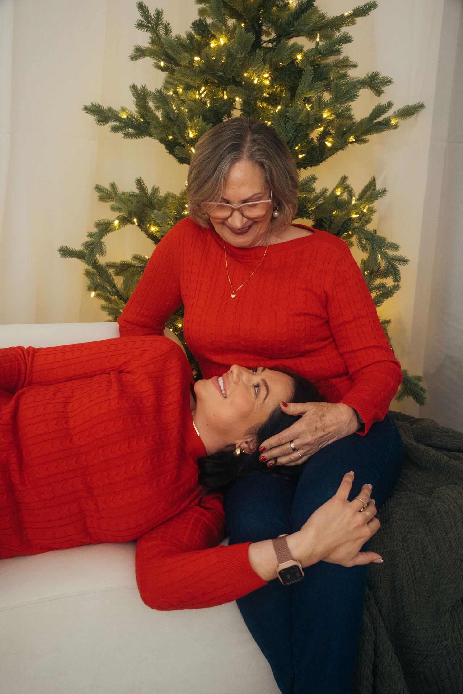 Two people in matching red sweaters share tender moment in front of Christmas tree with twinkling lights.