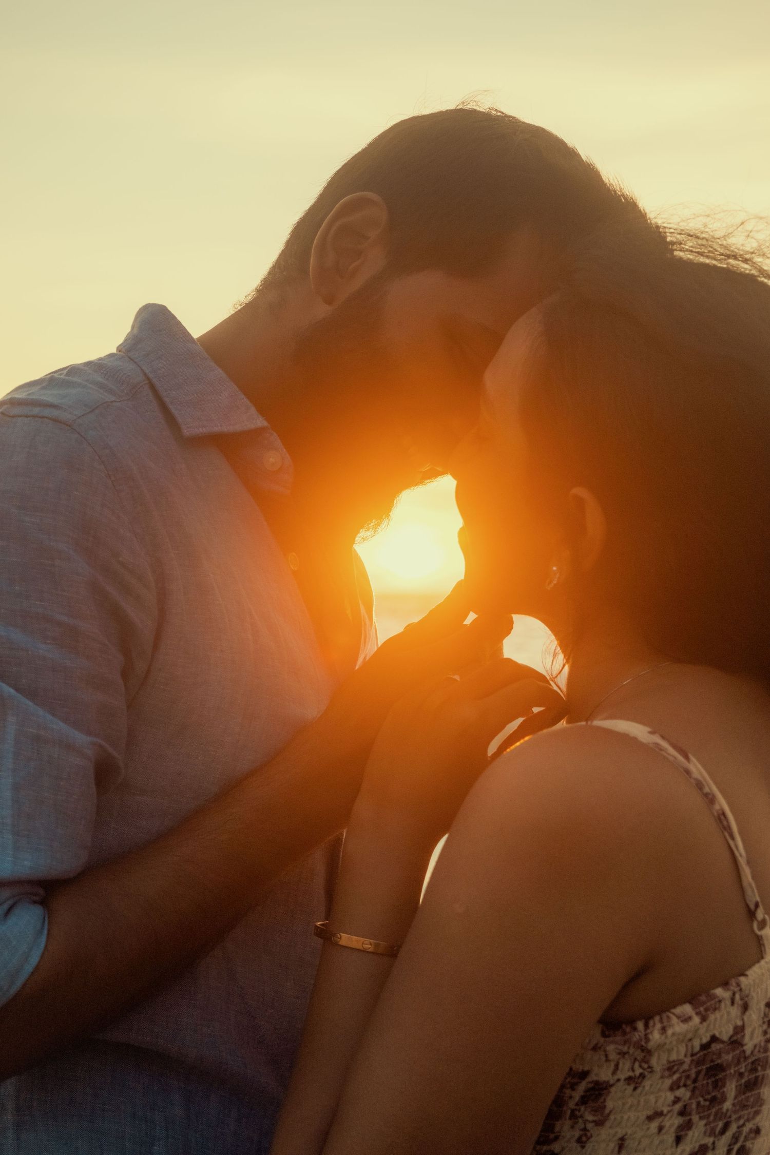 Romantic couple sharing an intimate moment at golden sunset, silhouetted against warm glowing light.