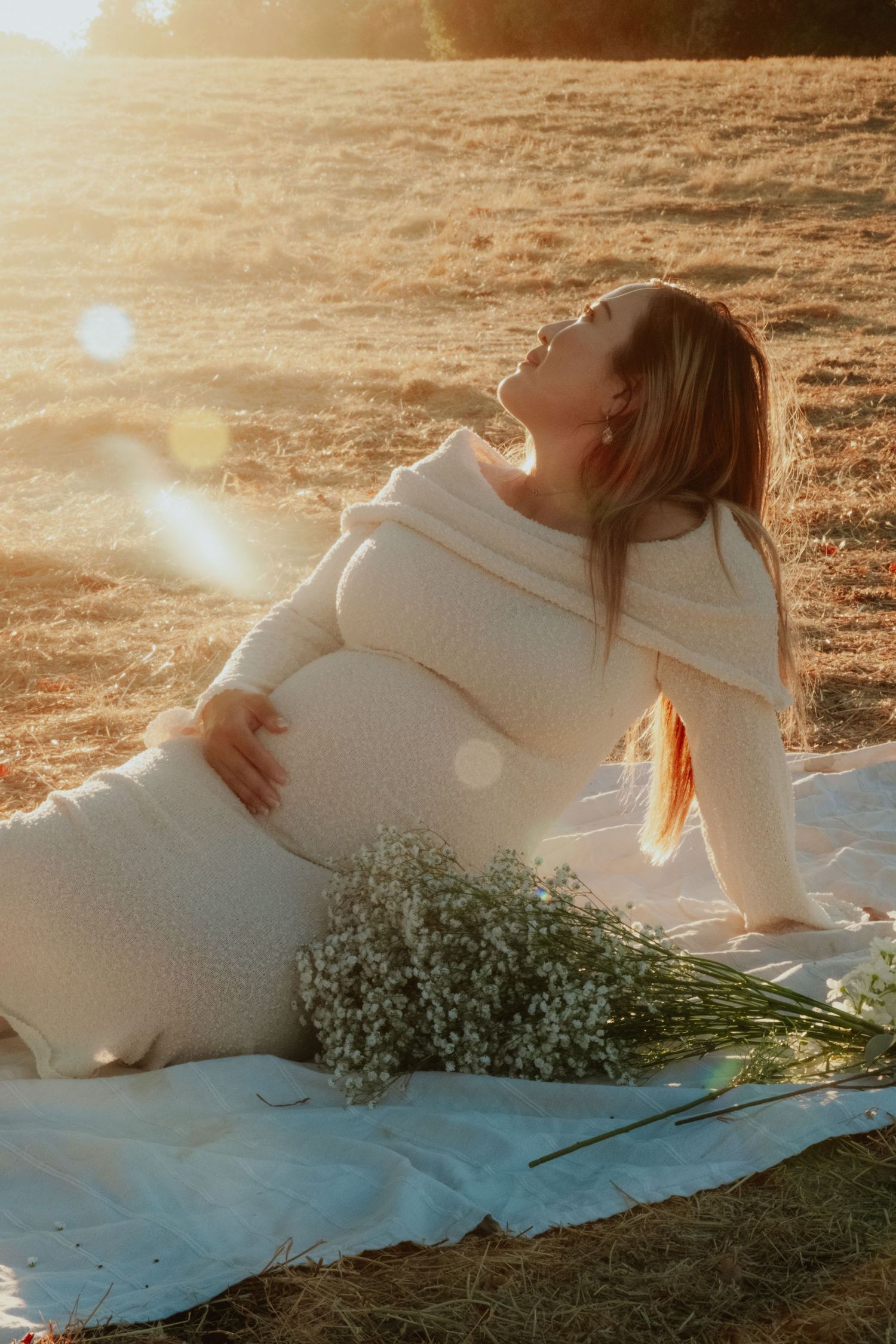 Dreamy maternity photoshoot in golden sunlight with baby's breath flowers.