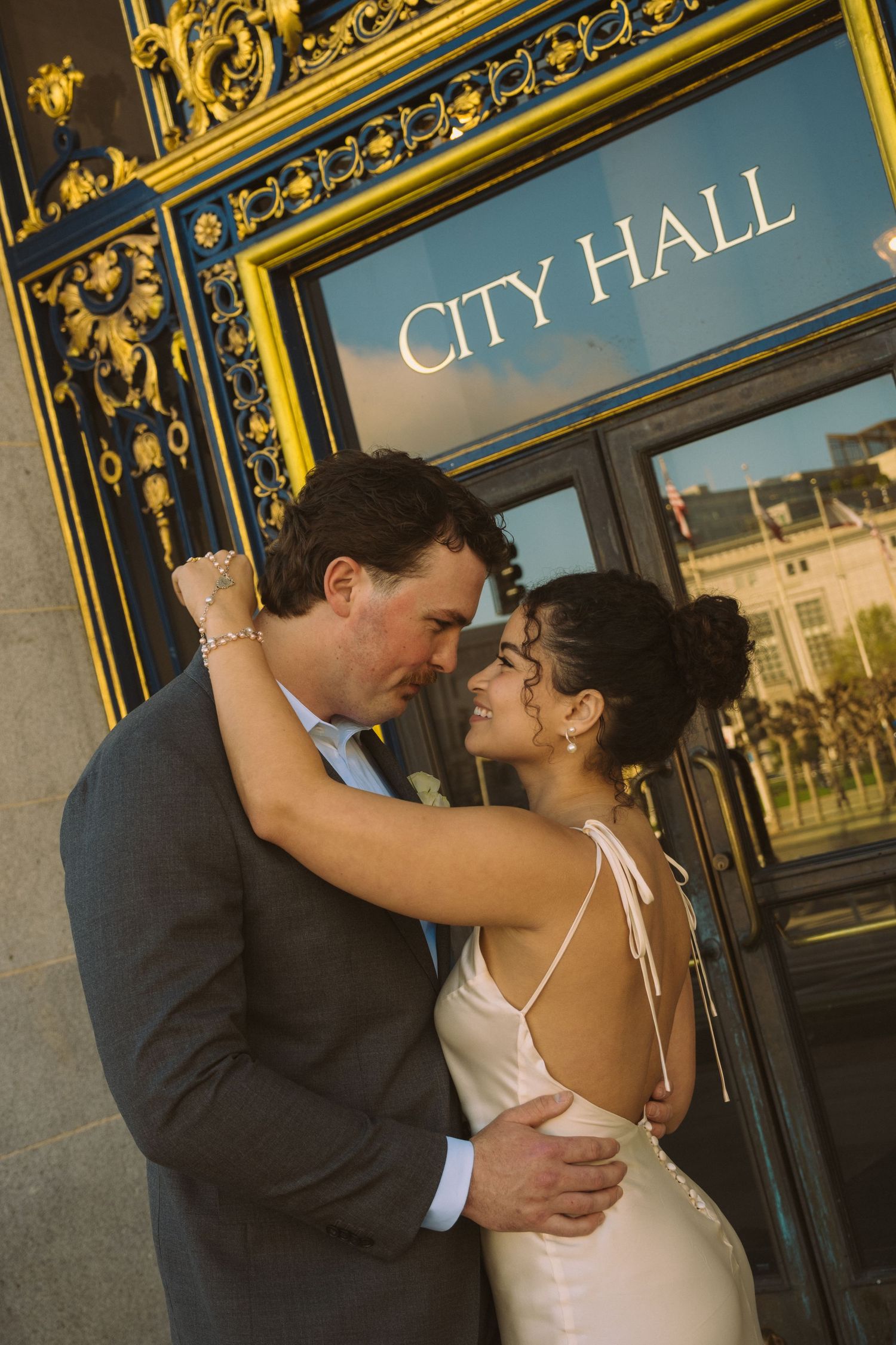 Couple embracing and smiling in front of San Francisco City Hall golden doors after their wedding ceremony.