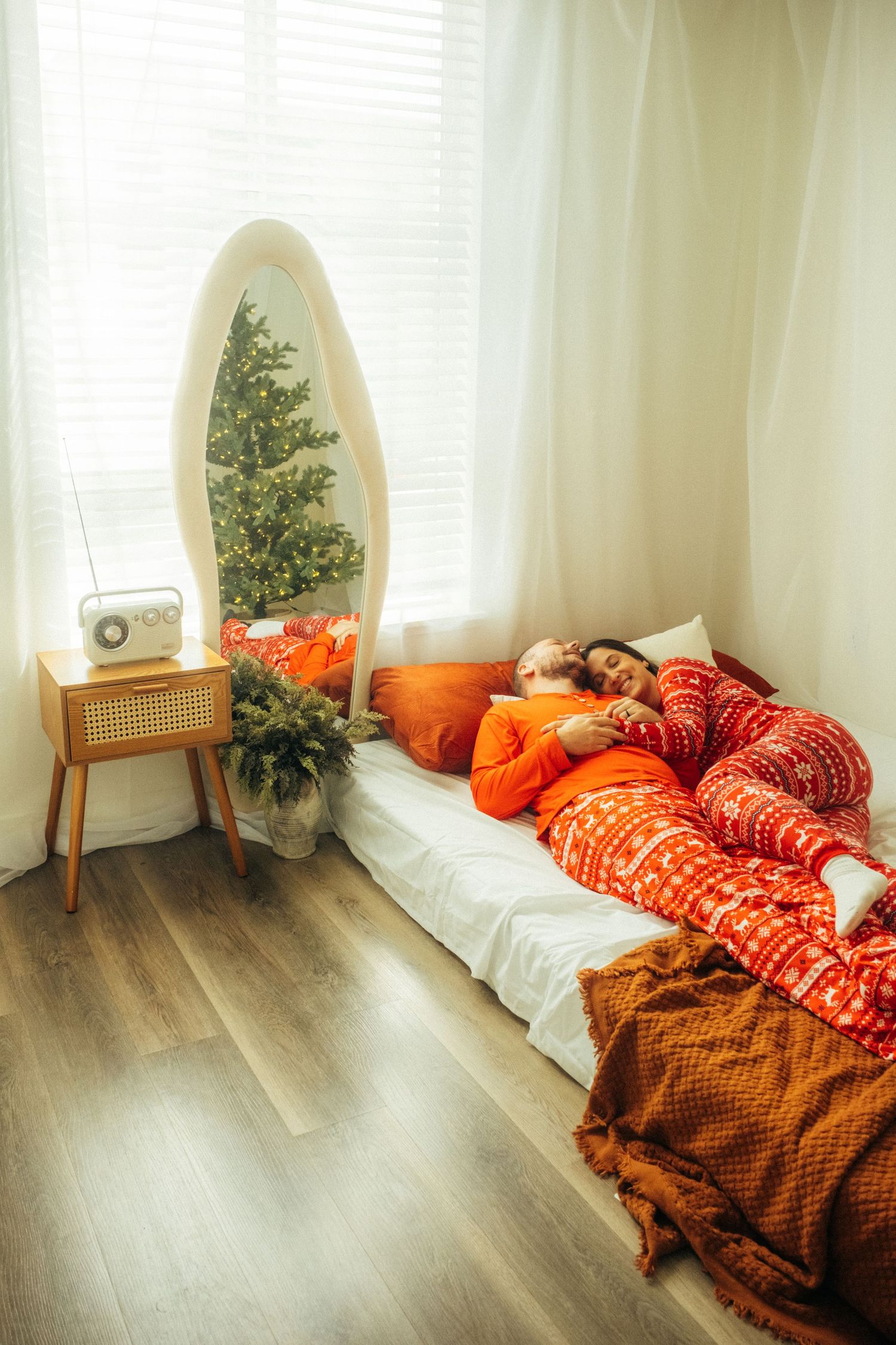 A cozy bedroom setup with Christmas decor, featuring a mirror, tree, and red holiday bedding.