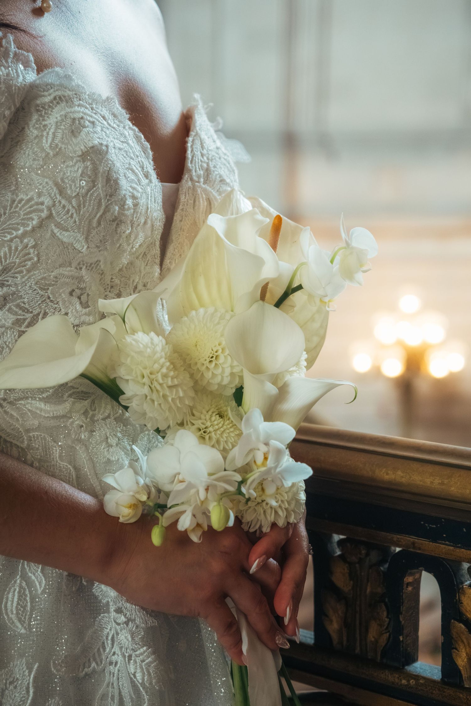 Close-up of white wedding bouquet with orchids and dahlias against lace dress.