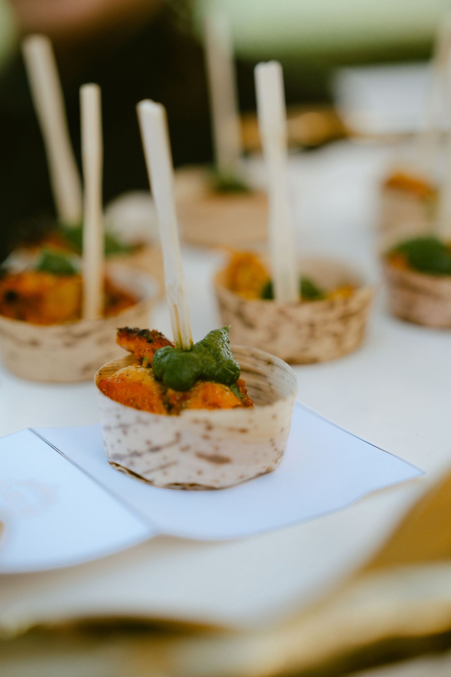 Elegant appetizer cups with roasted vegetables, fresh basil, and decorative skewers served at a catered event.