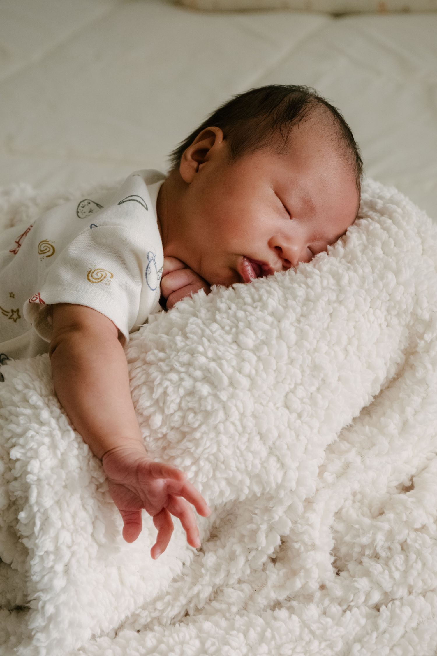 Sleeping infant on fluffy white blanket with hand outstretched.